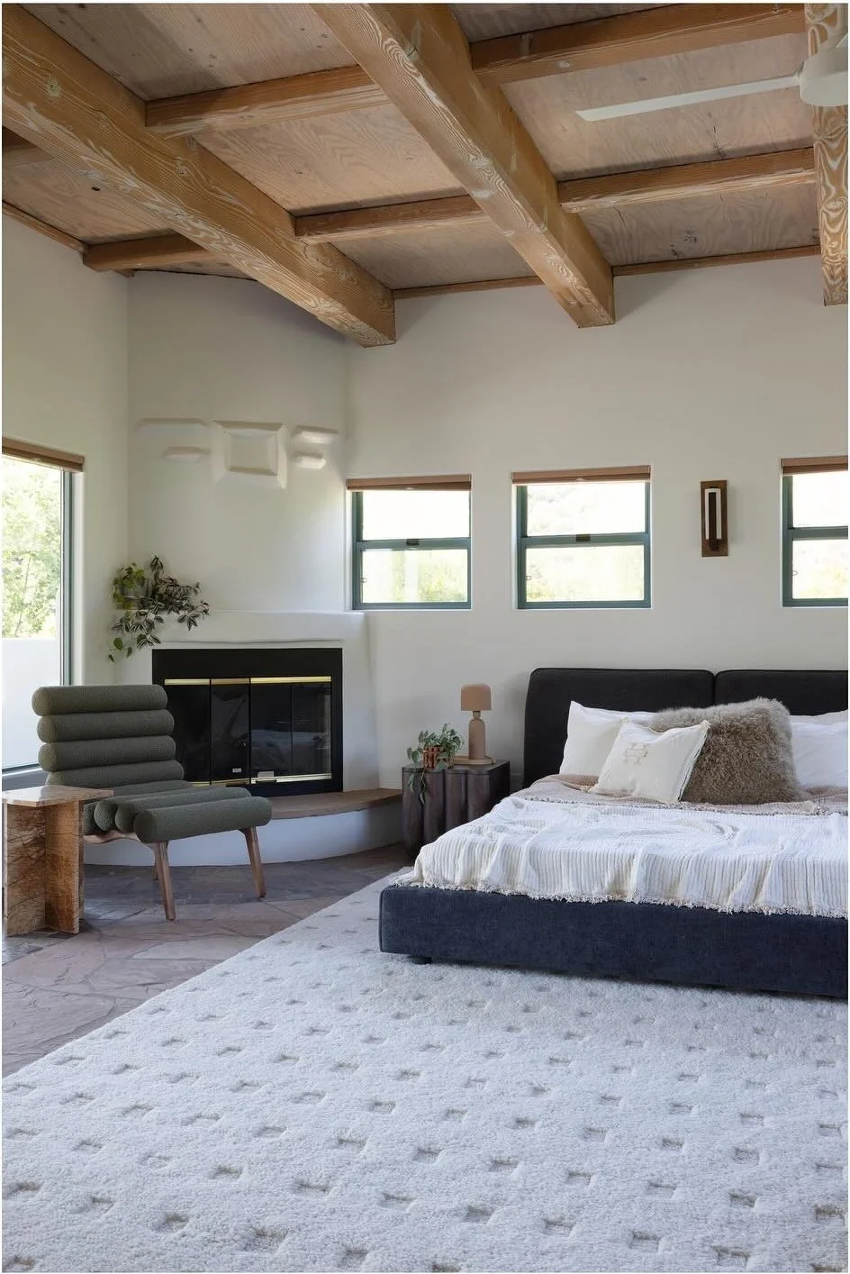 Pale patterned wool rug beneath a bed beside a wood stove
