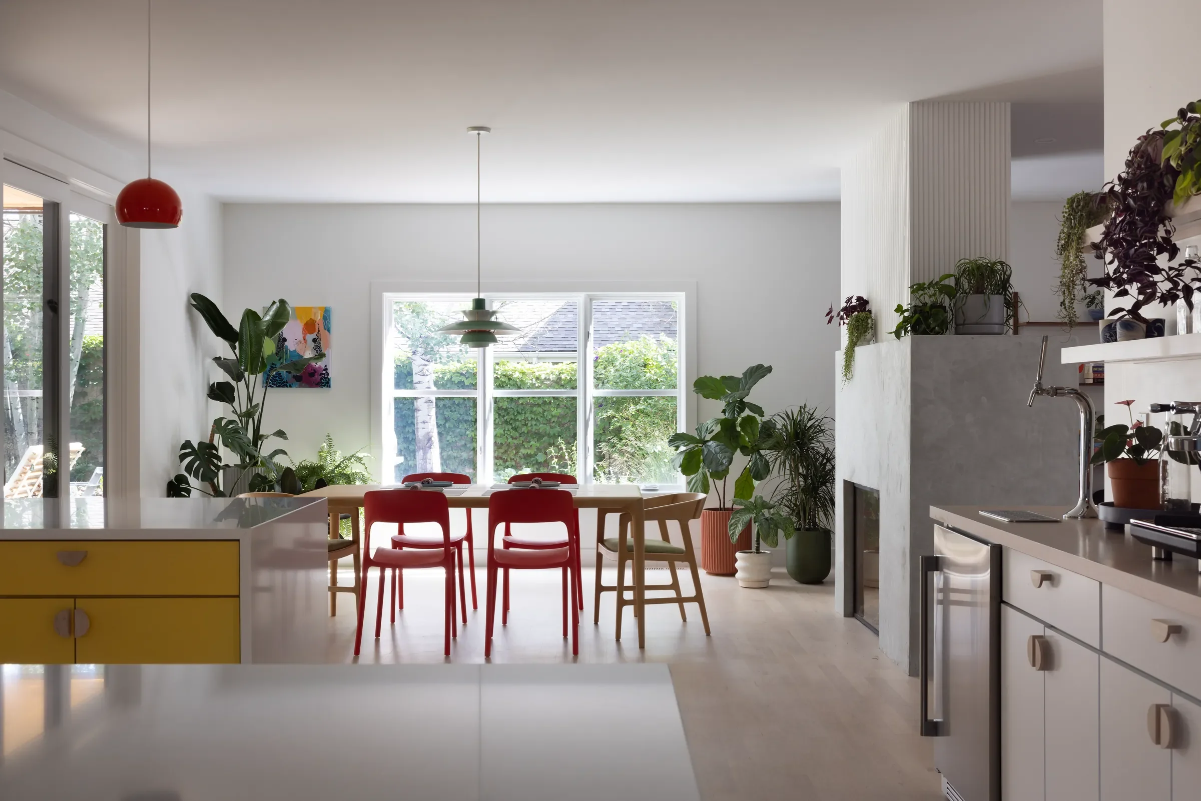 Open-plan kitchen and dining room with red chairs, large windows, and plants.