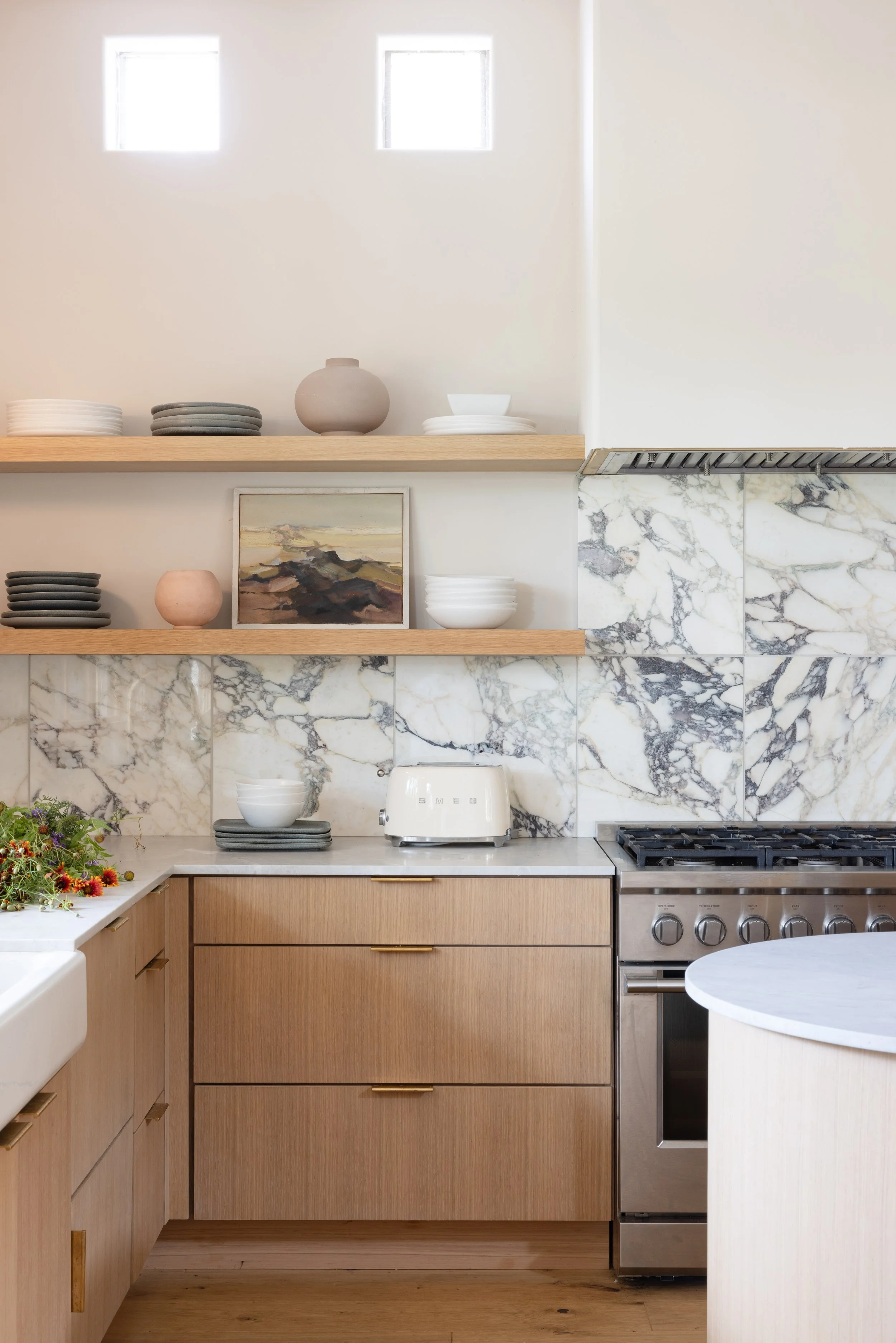 Kitchen with light wood cabinetry, open shelves, and veined marble backsplash.