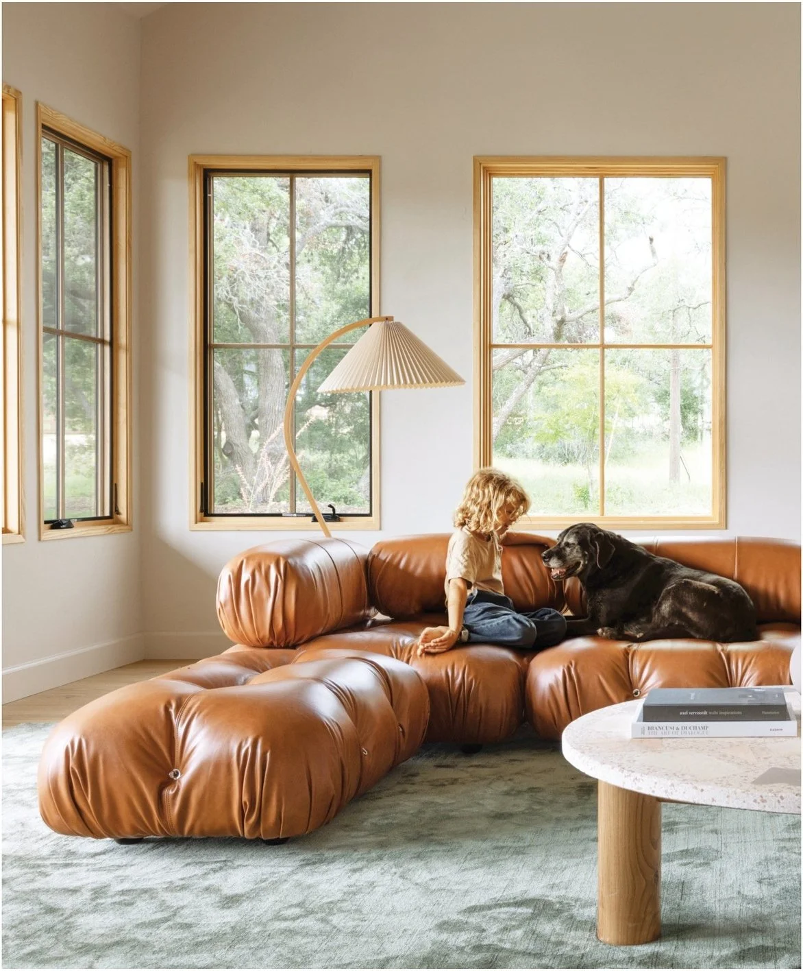 Caramel leather seating and a round stone table beside tall windows