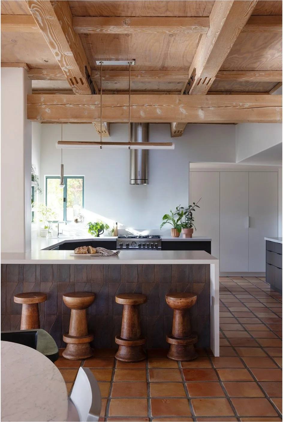 Renovated kitchen island beneath heavy wood beams above Saltillo flooring