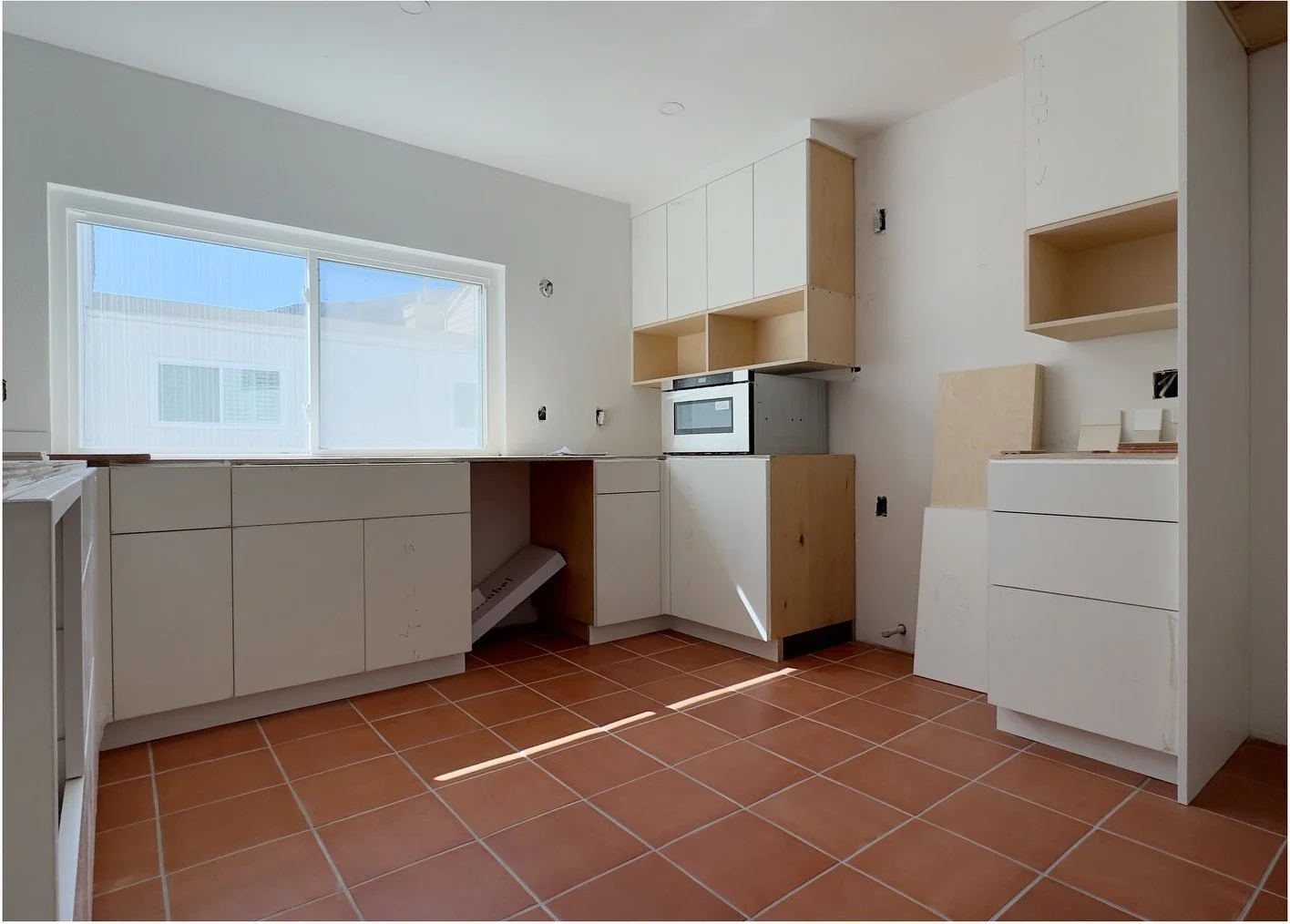 Original pale kitchen with terracotta flooring and a small window