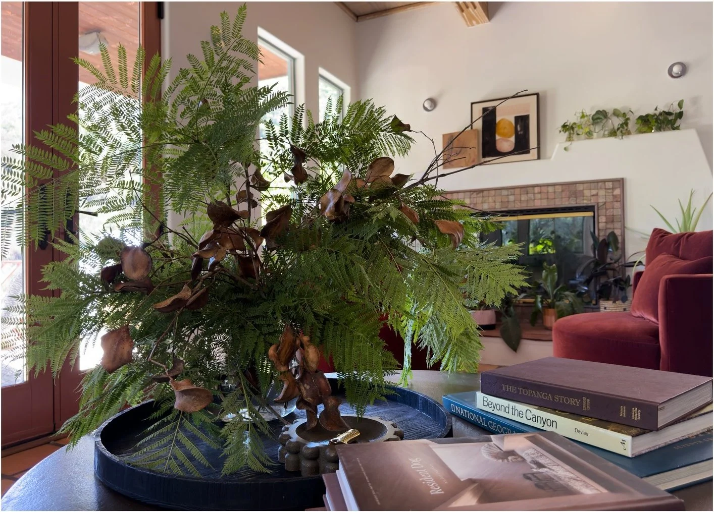 Large leafy arrangement beside a burgundy chair and framed artwork