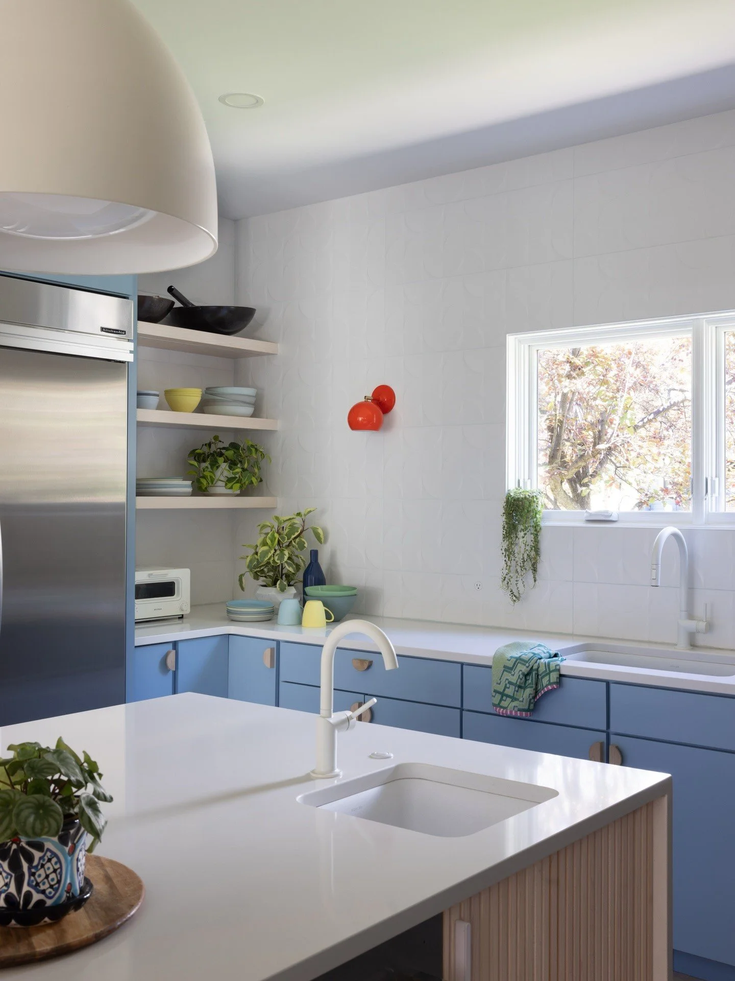 Blue kitchen cabinets beside a white island and leafy window