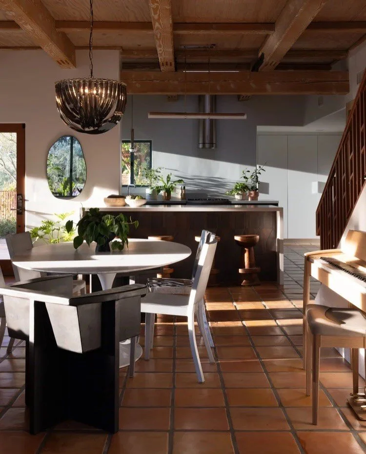 Round dining table beside a dark kitchen island and wood beams