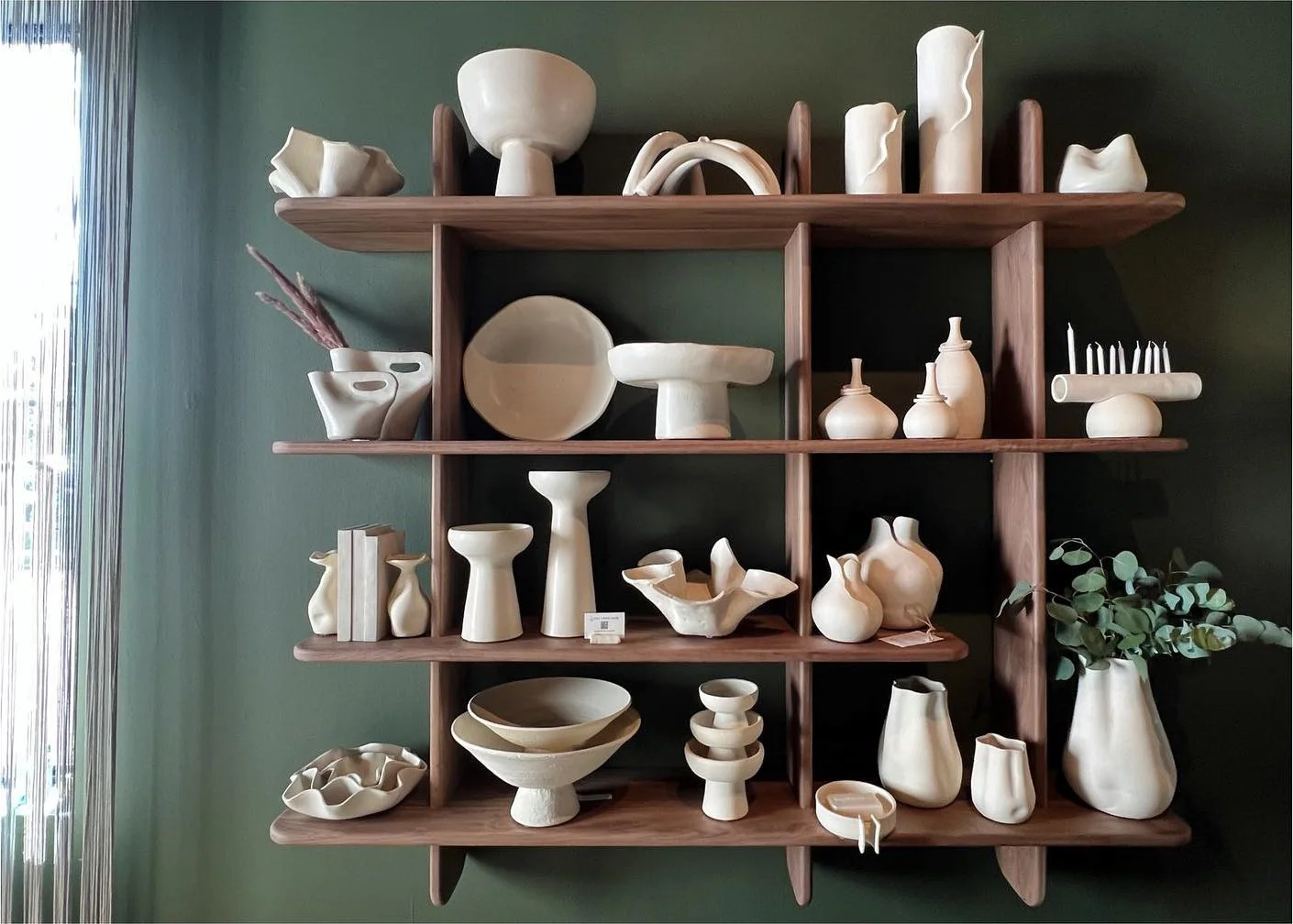 Open wood shelving filled with ceramic bowls vessels and sculptural objects