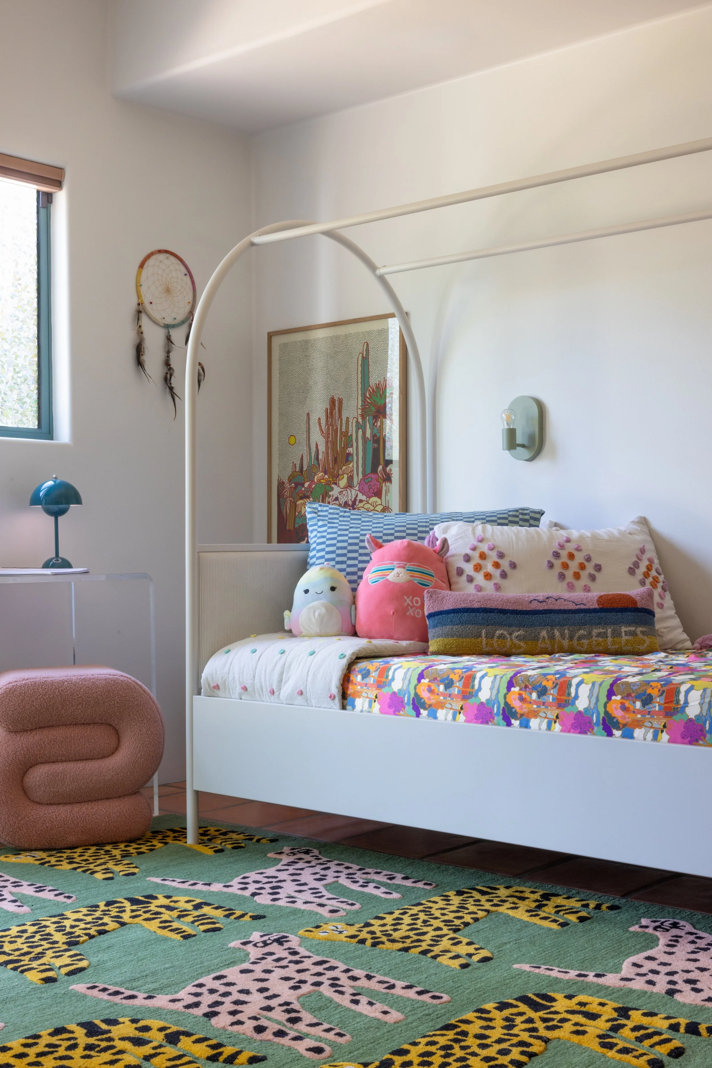 Child’s bedroom with a colorful quilt, pink chair, and patterned rug.