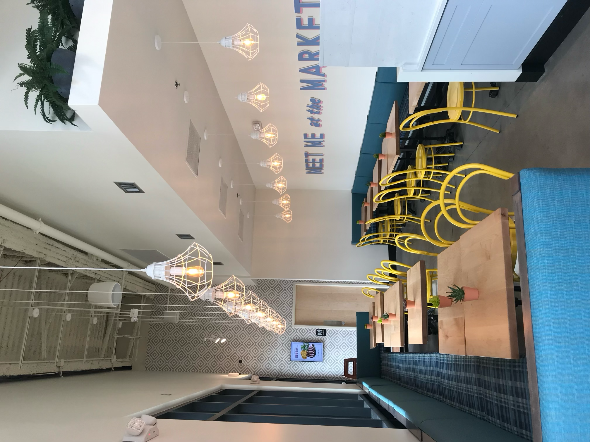 Restaurant dining room with blue banquettes, yellow chairs, and hanging wire lights.