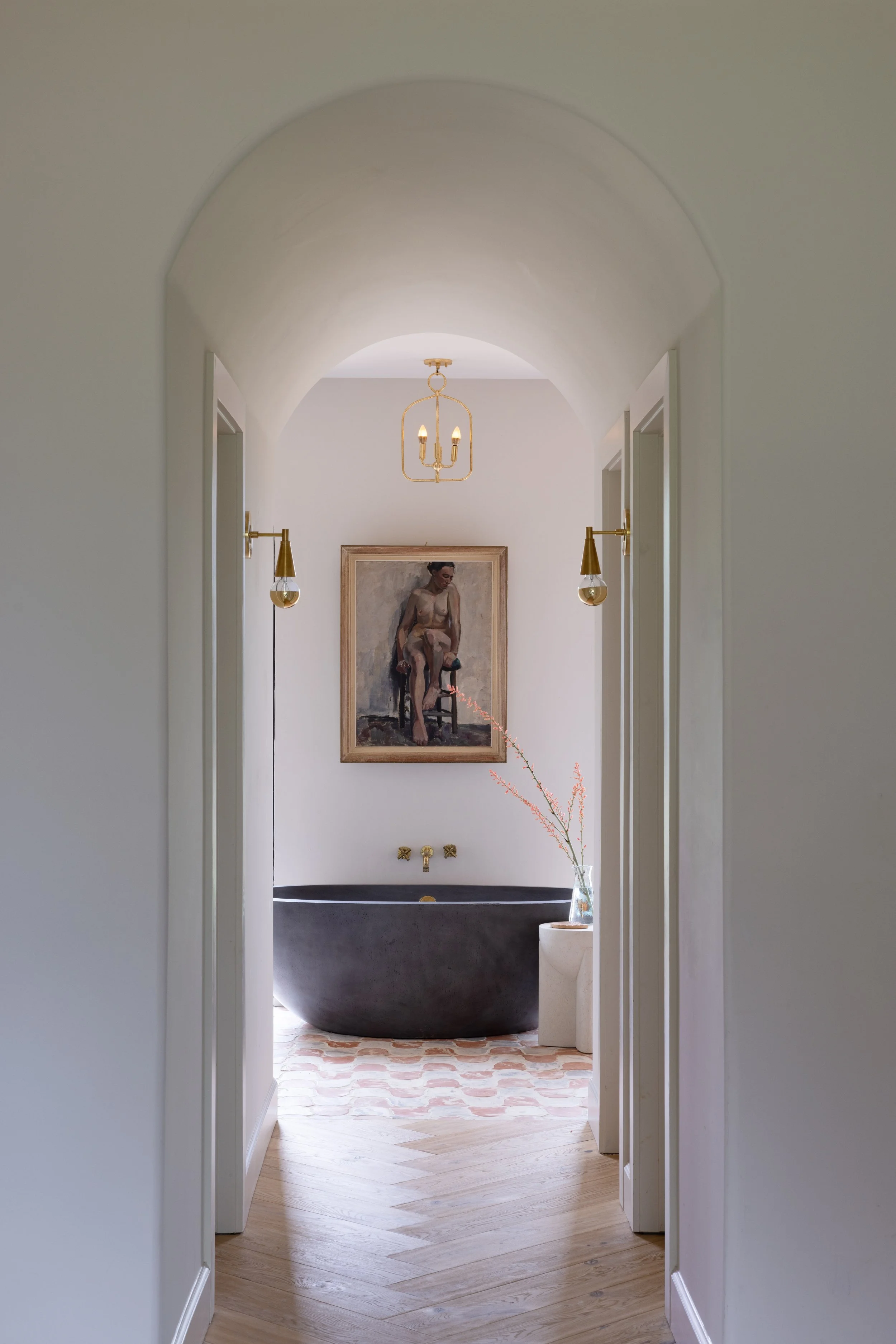View through an arched hallway to a dark freestanding bathtub and framed art.