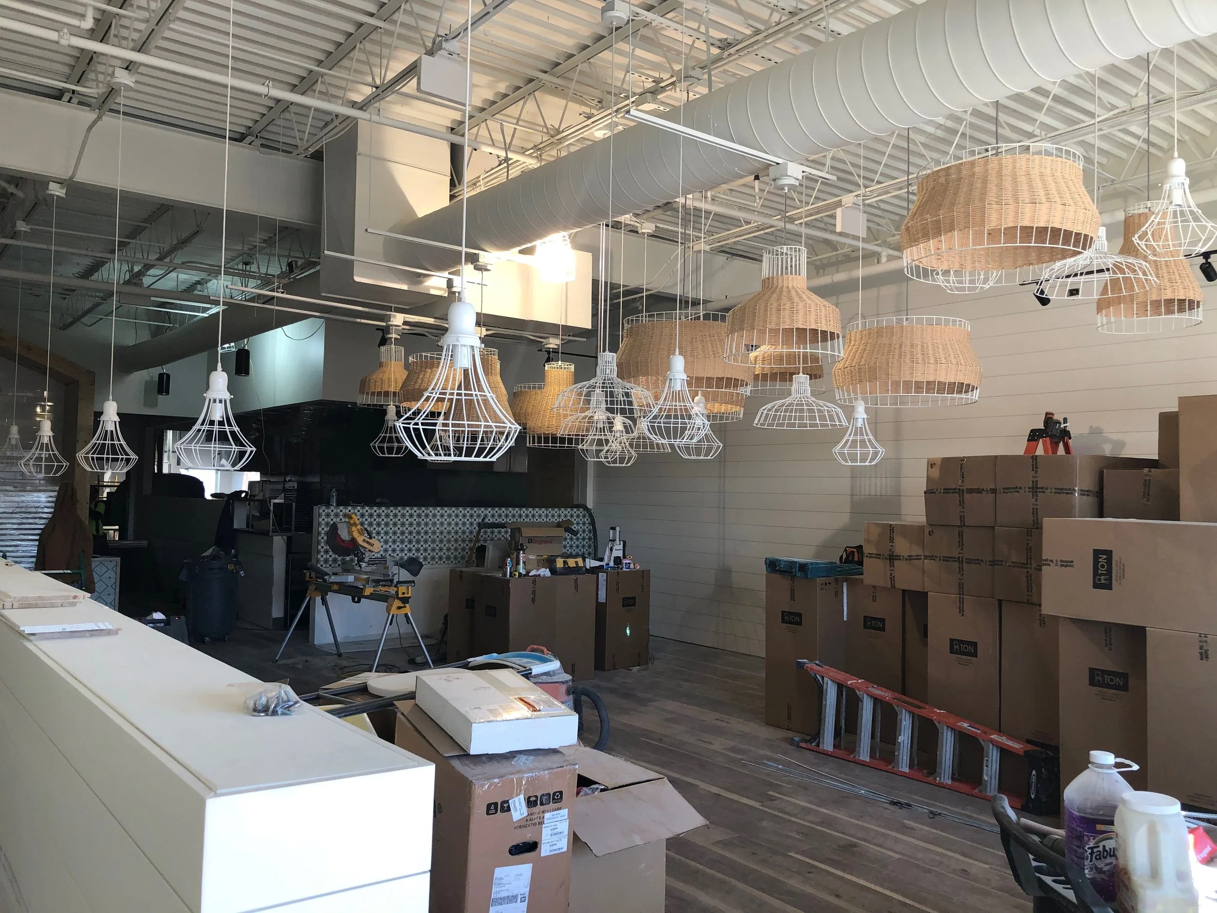 Restaurant interior under construction with pendant lights, exposed ducts, and stacked boxes.