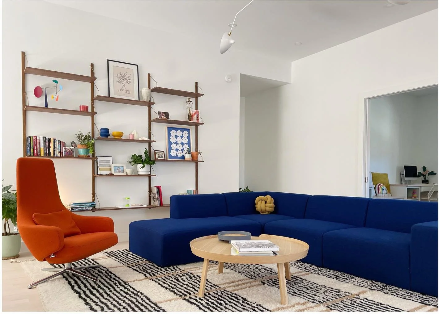 Blue sectional and orange lounge chair beside a round pale coffee table
