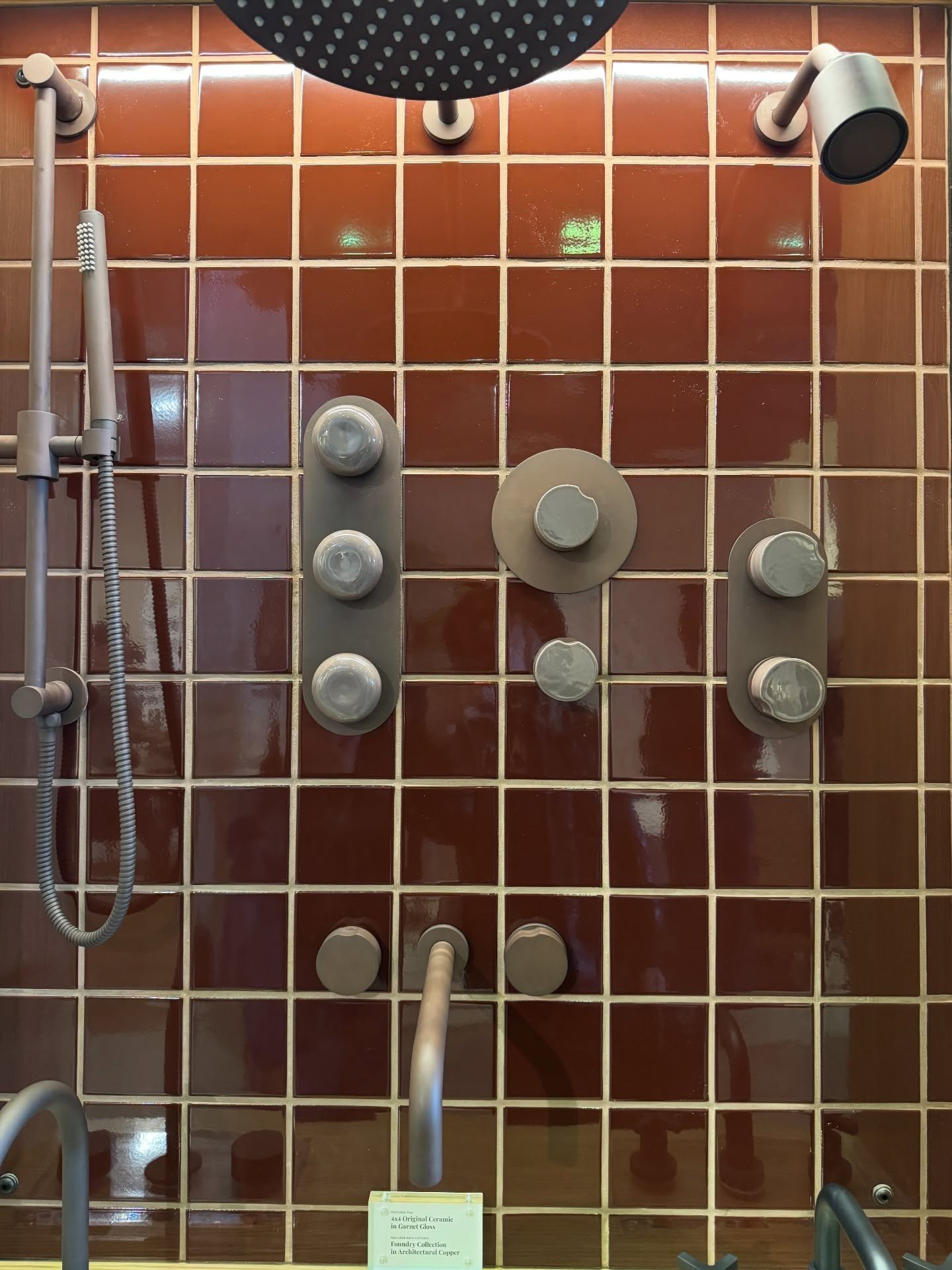 Shower fixture display against glossy reddish square tile
