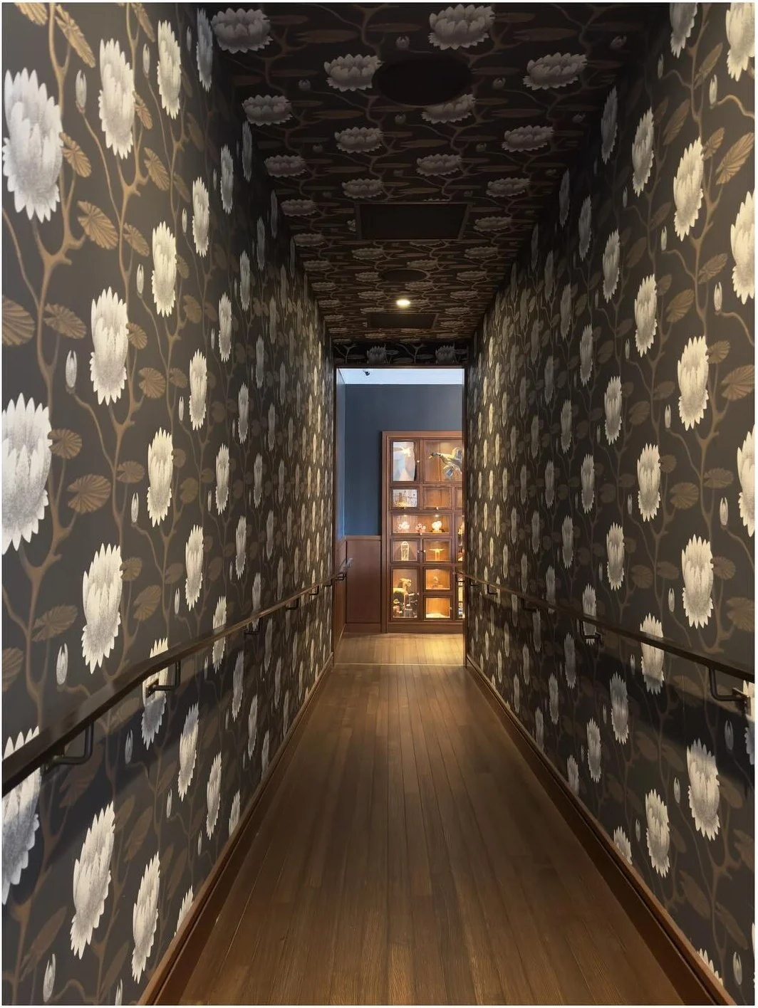 Dark floral wallpaper covering a long timber-floored hallway