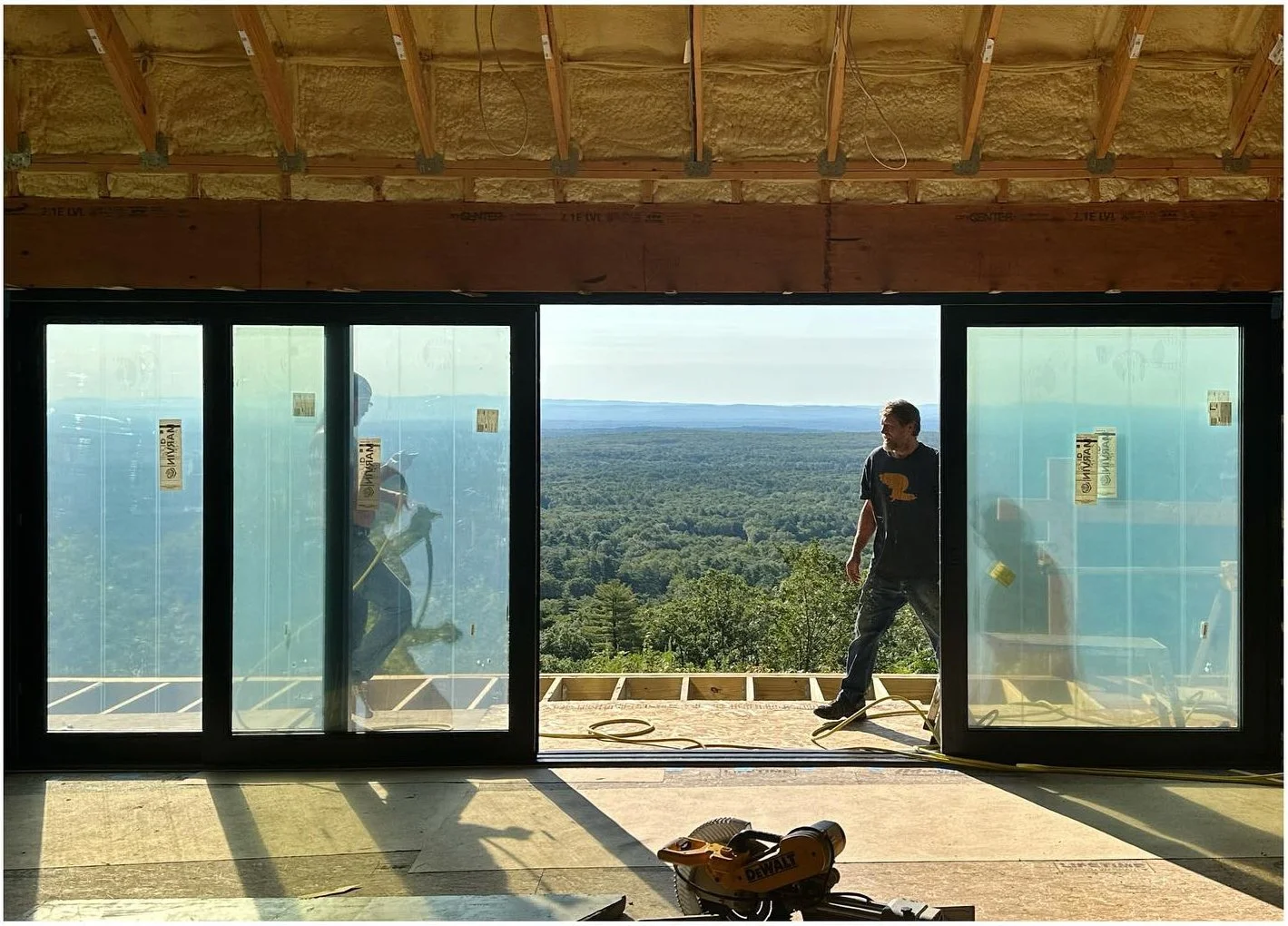 Worker beside large glazed doors overlooking wooded hills during construction