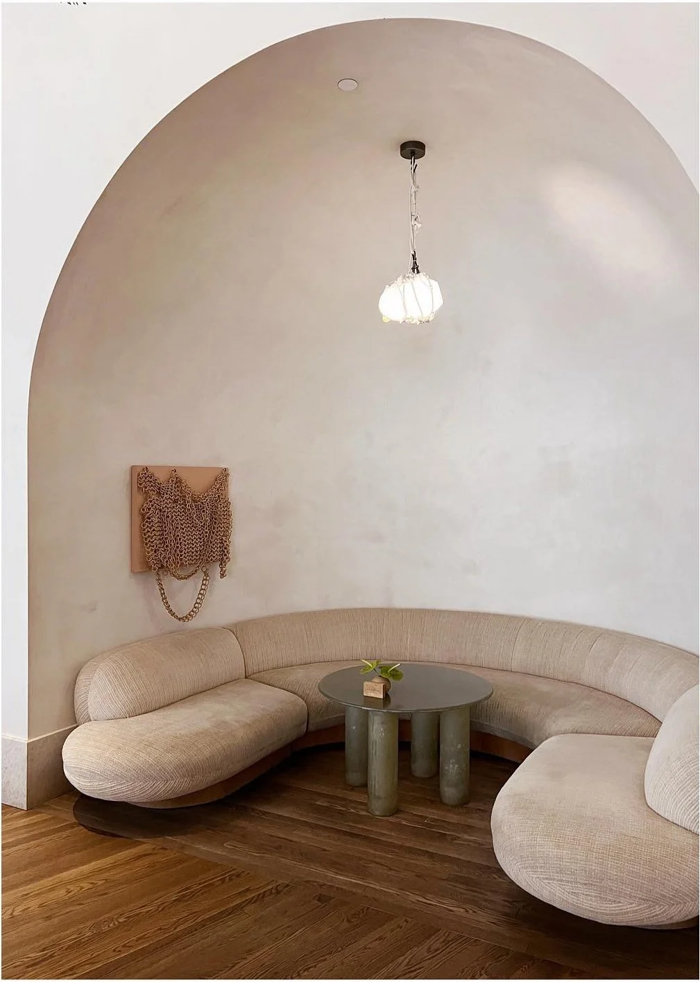 Curved pale sofa inside a tall white arch with pendant lighting