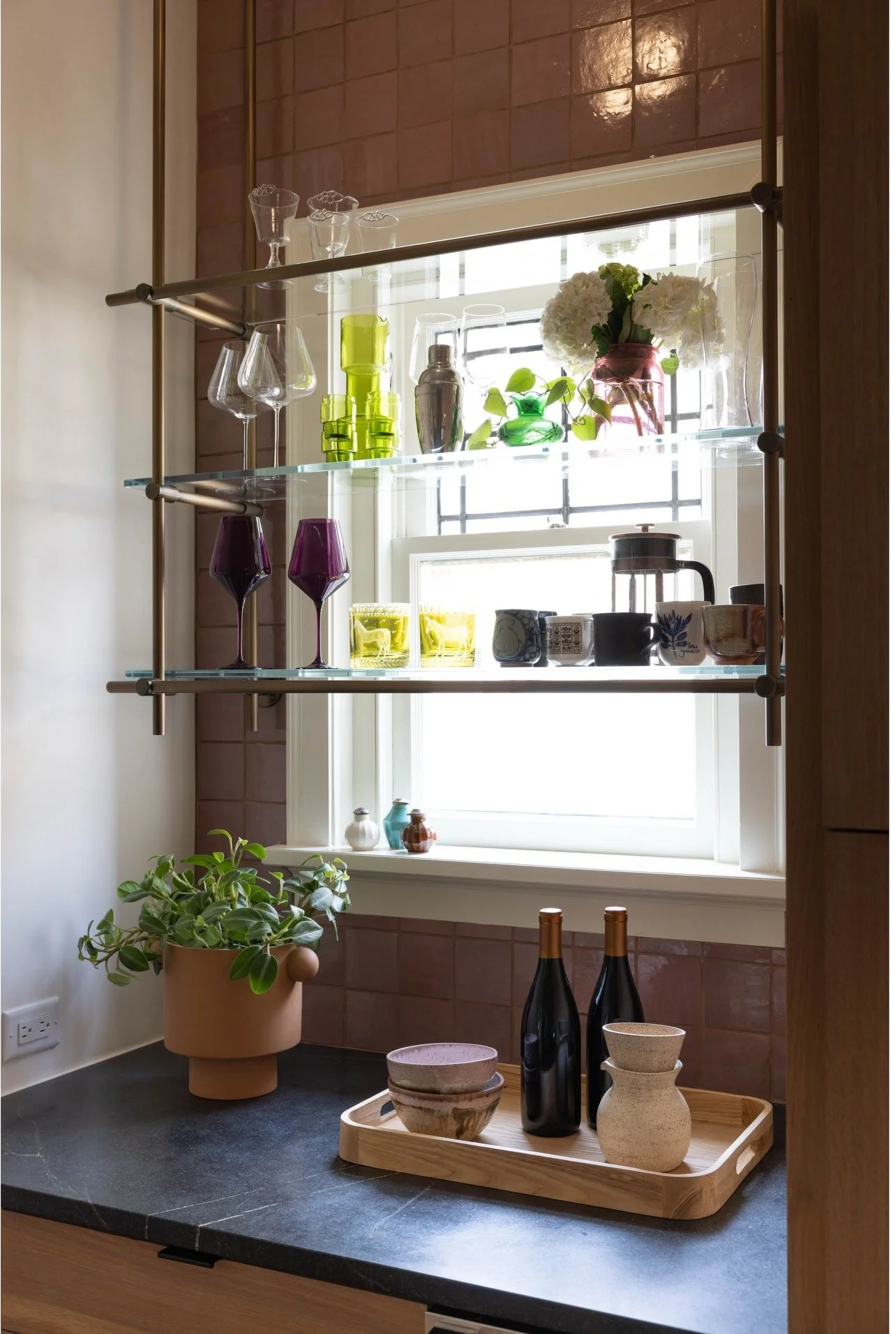 Window shelves displaying colorful glassware above a dark countertop
