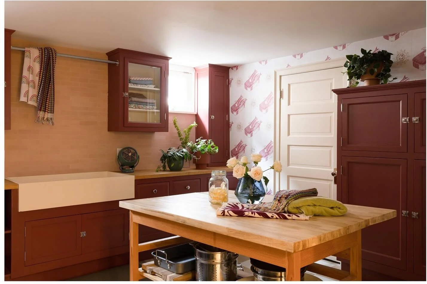 Laundry room with burgundy cabinets wood table and illustrated wallpaper