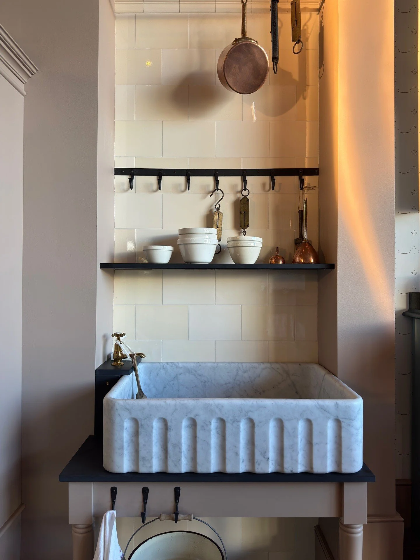 Fluted stone sink beneath copper pans and open shelves