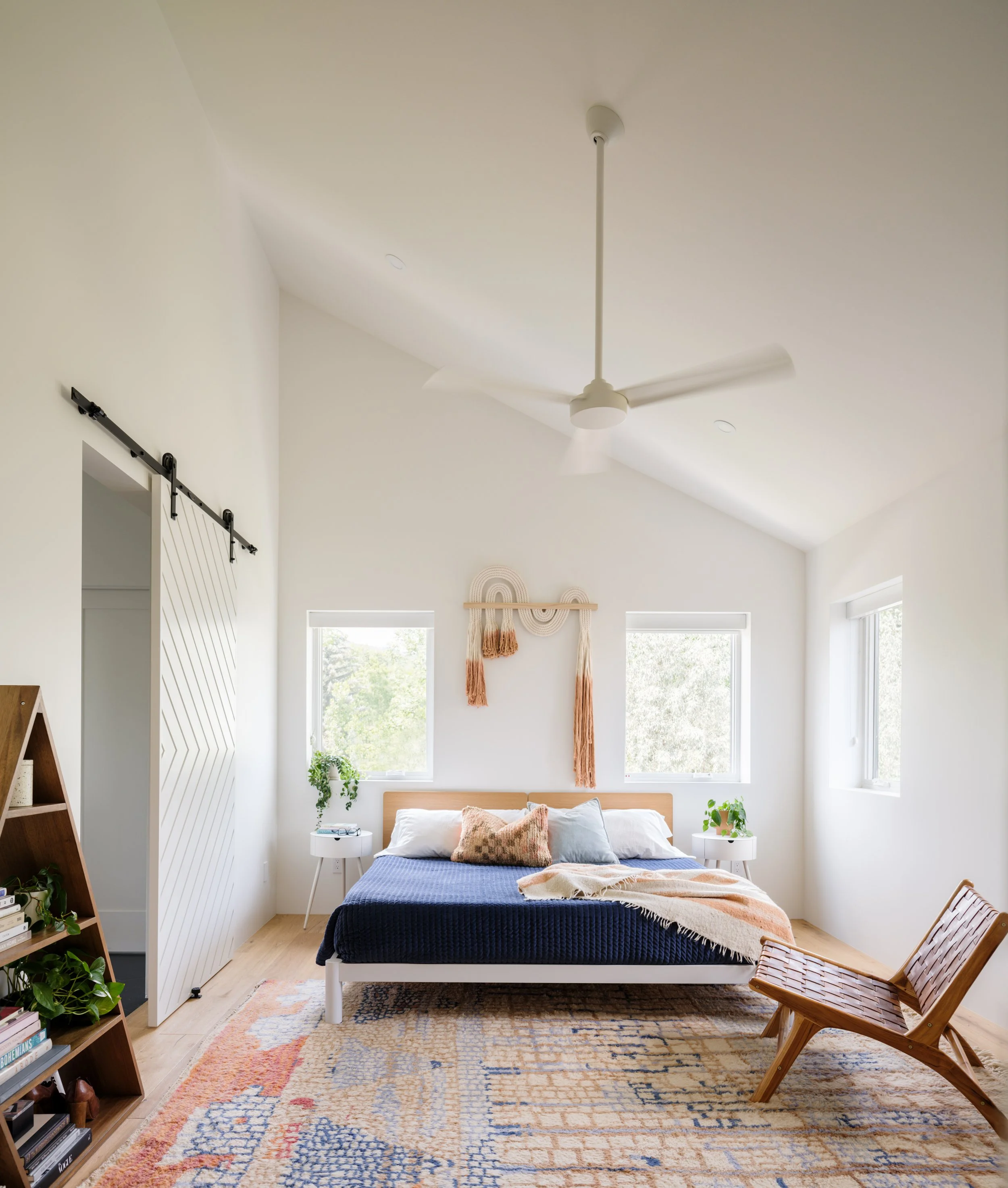 Bedroom with a vaulted ceiling, blue bed, wood chair, and patterned rug.