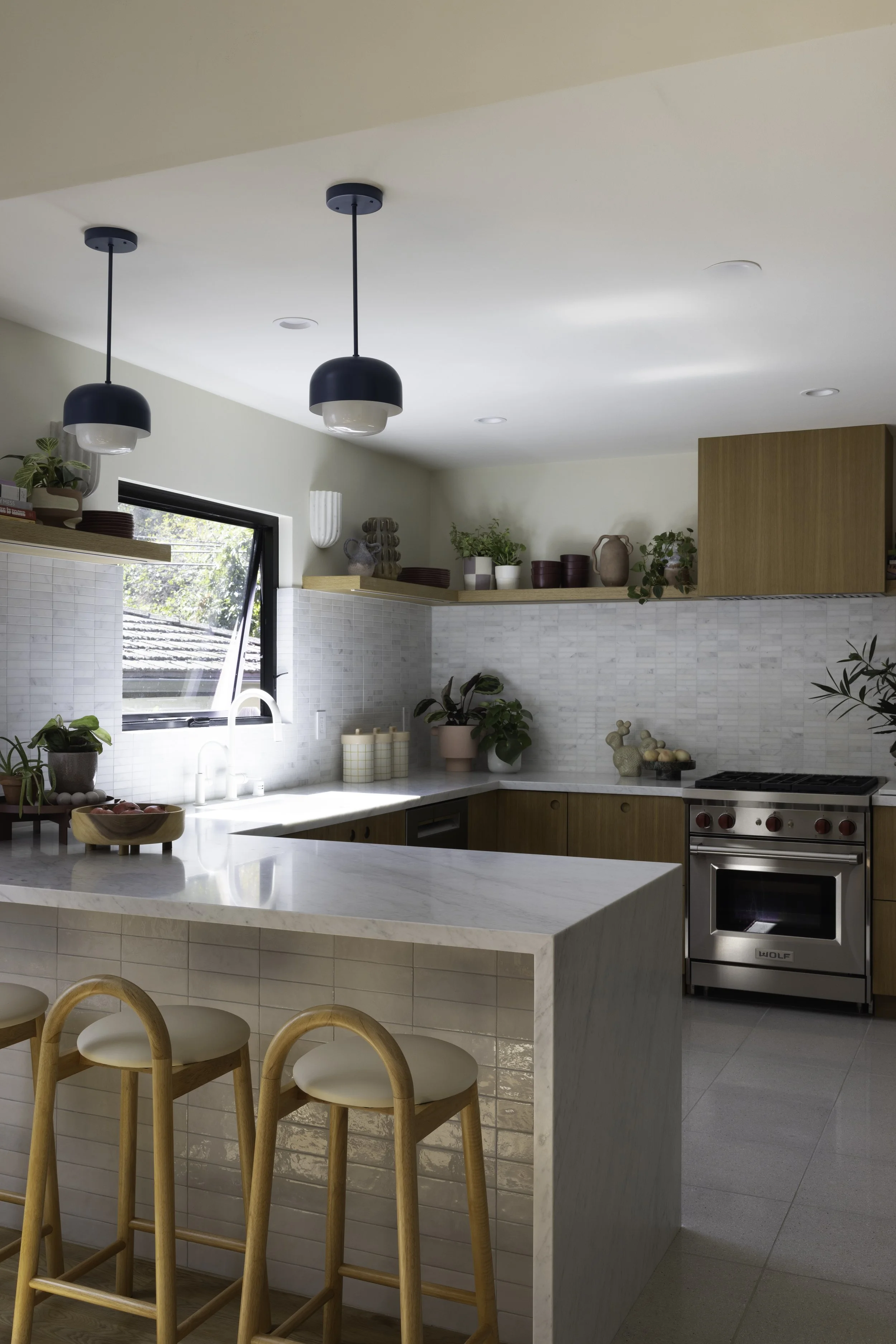 Kitchen with a white island, yellow stools, wood cabinets, and pendant lights.