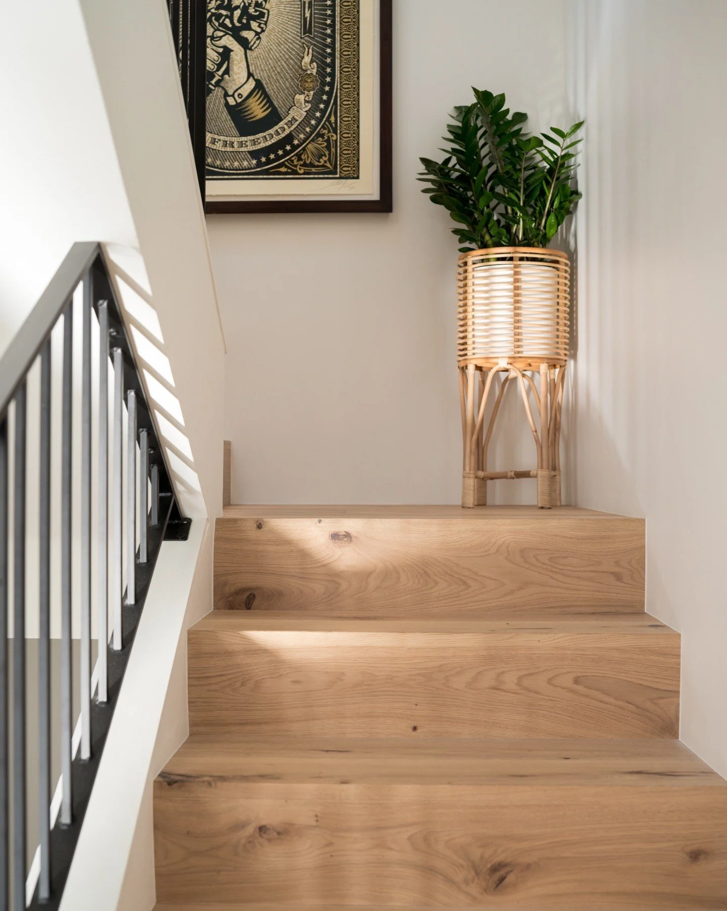 Pale wood steps with black rails and a plant on the landing