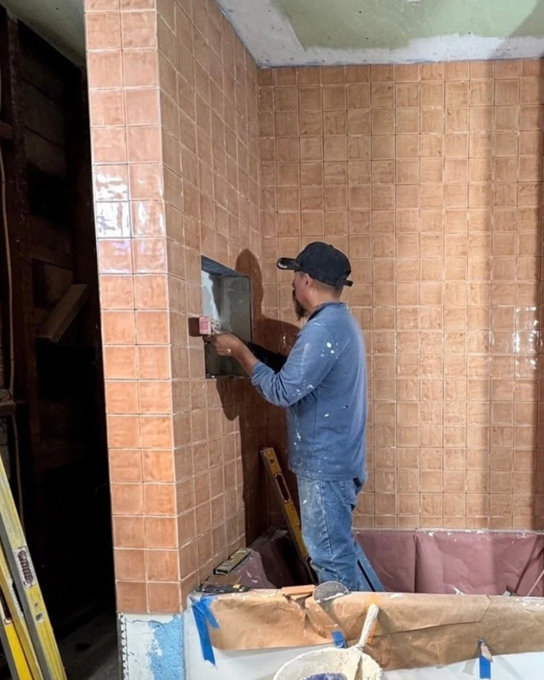 A contractor fitting peach tile on a bathroom wall