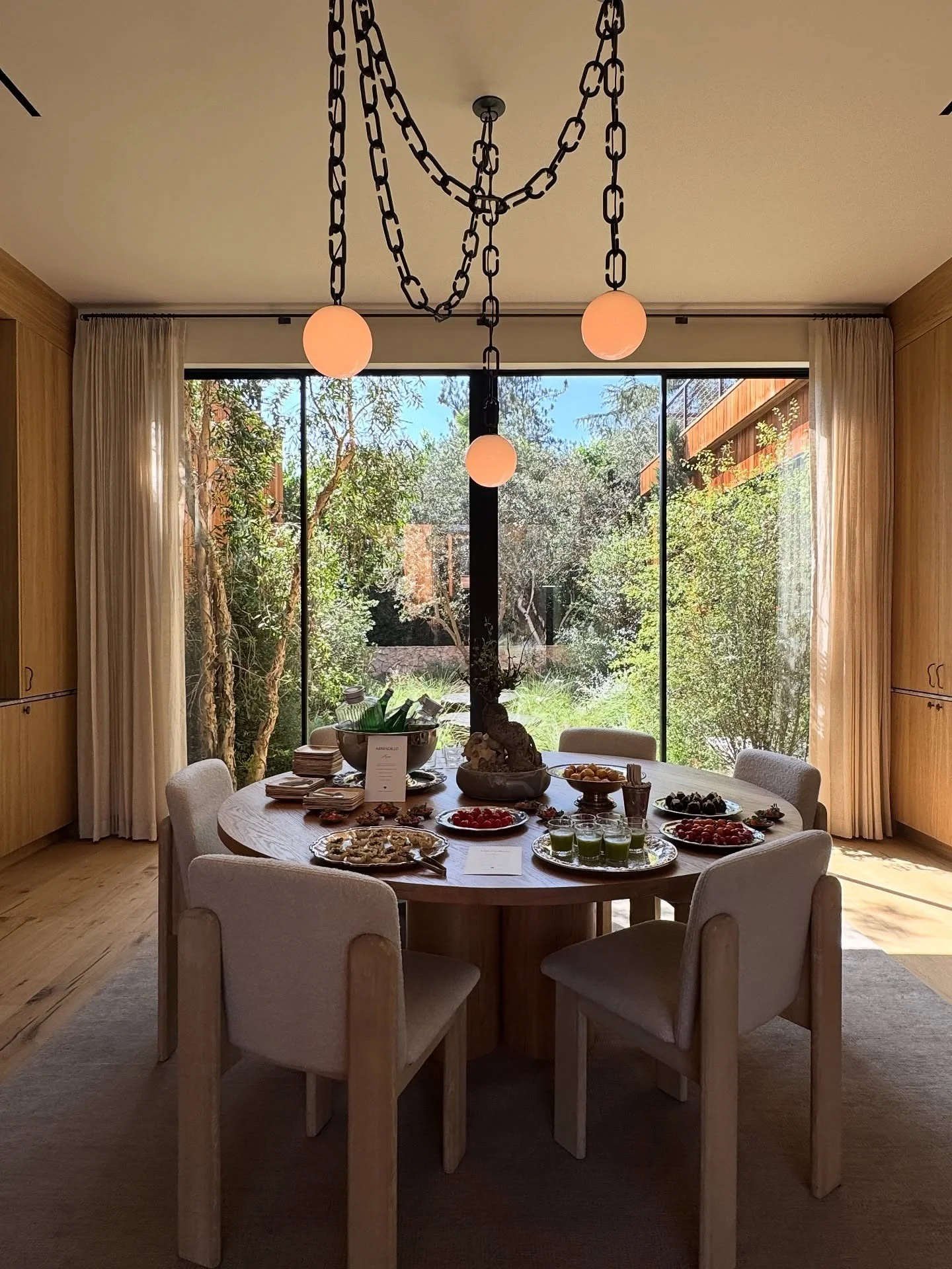 Round dining table beneath chain-hung globe lights beside a garden