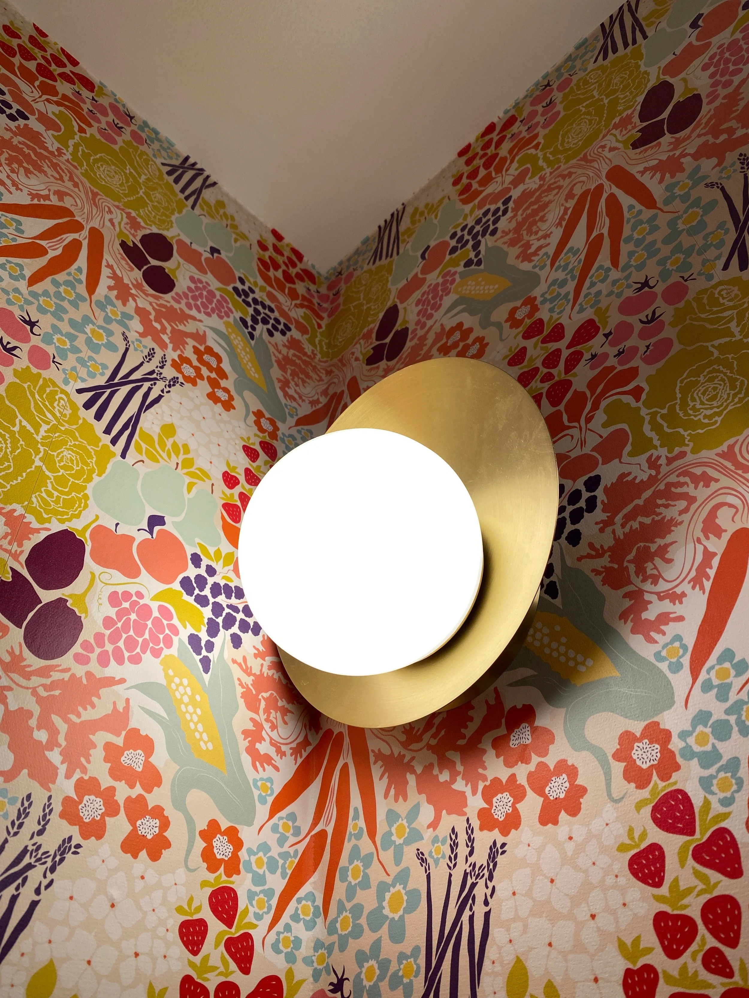 Round wall light against colorful floral wallpaper.