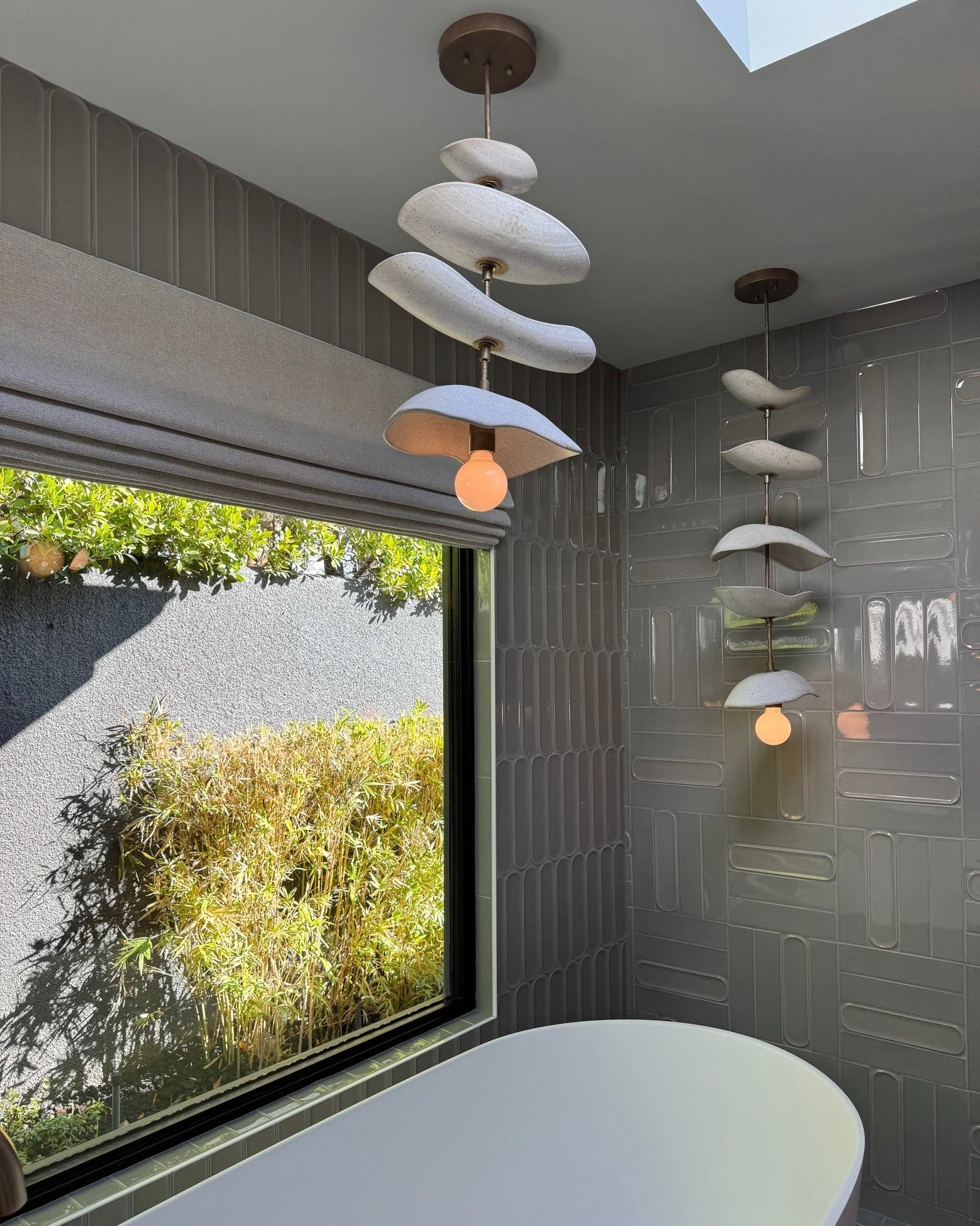 Freestanding bath beneath sculptural pendant lights beside a window