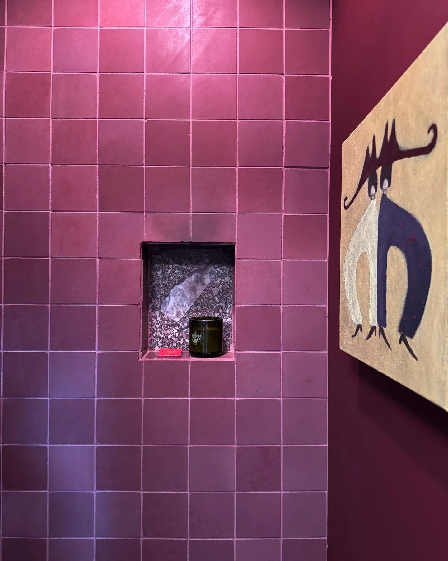 Pink tiled shower niche beside graphic cat artwork