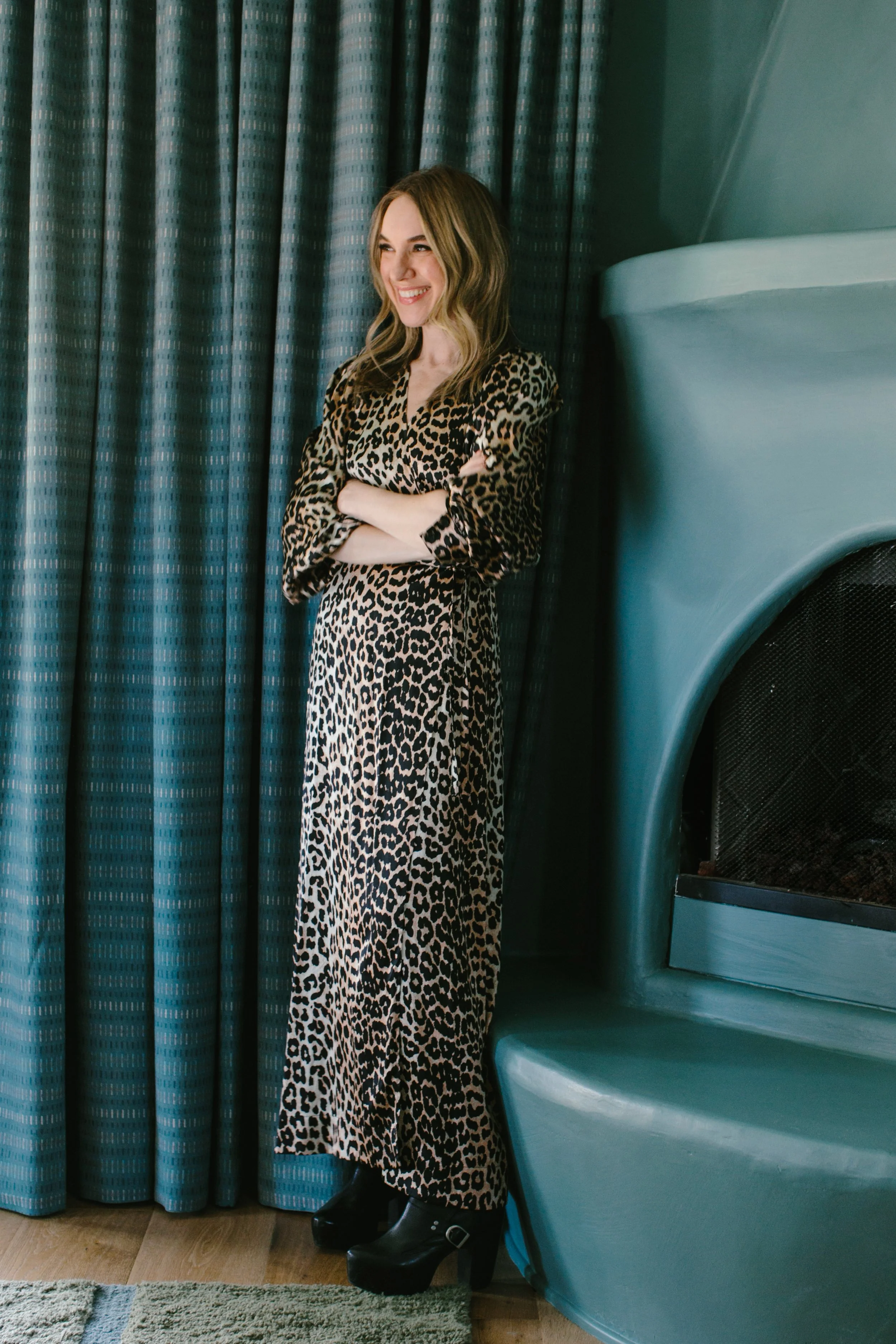 Amy Pigliacampo in a leopard-print dress beside a teal fireplace.