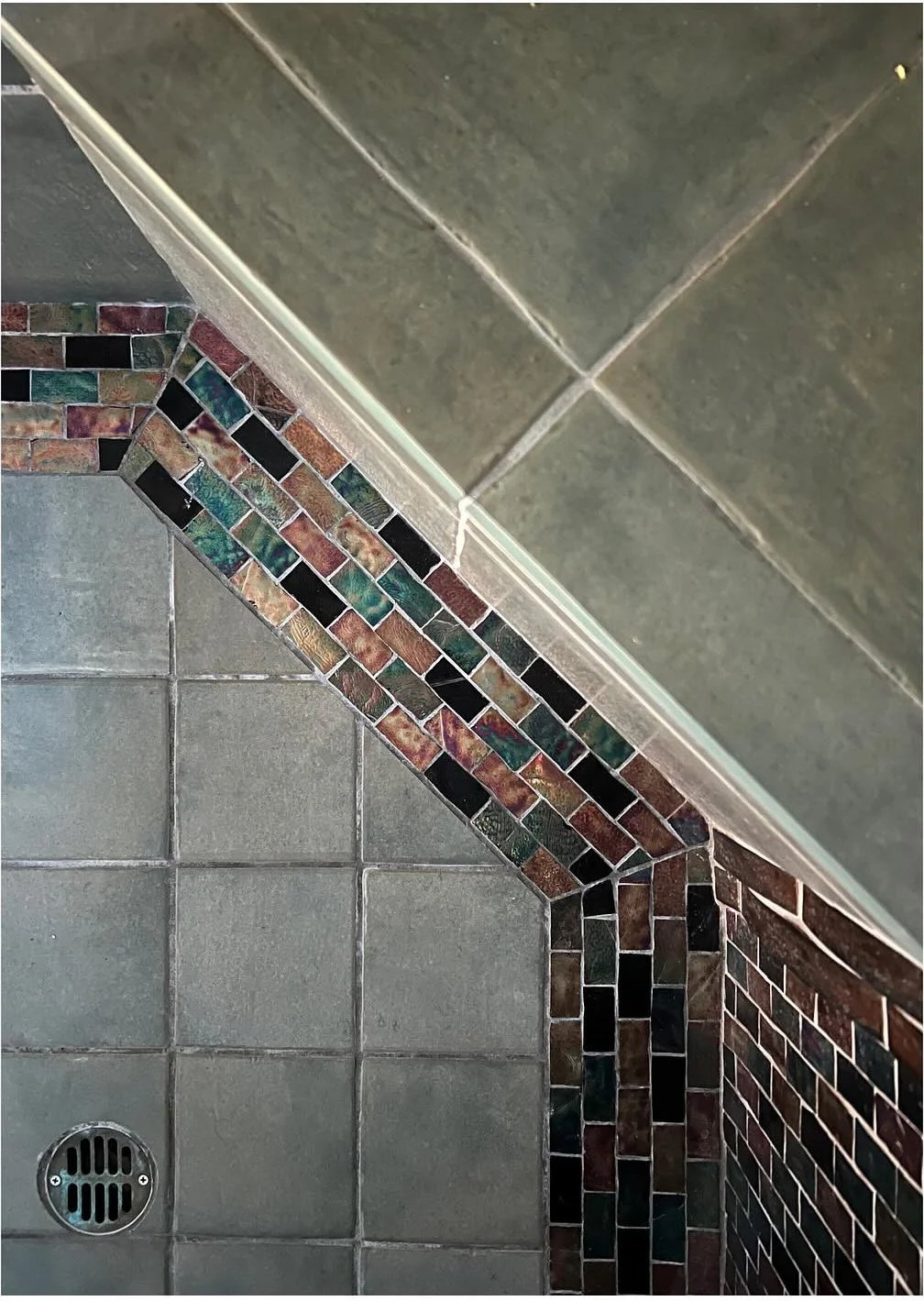 Diagonal mosaic border meeting large gray shower tiles