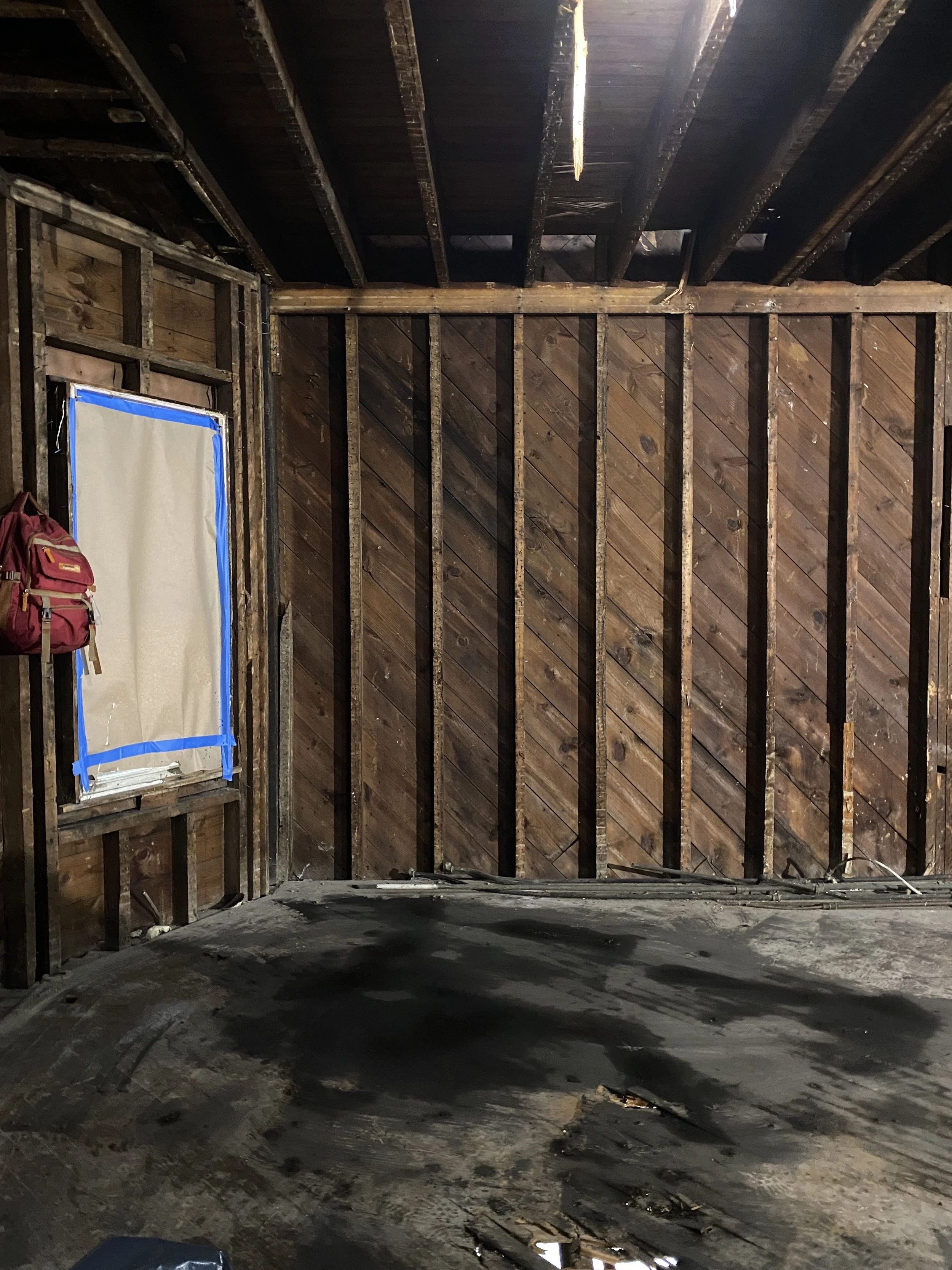 Room under demolition with exposed framing and a dark unfinished floor.