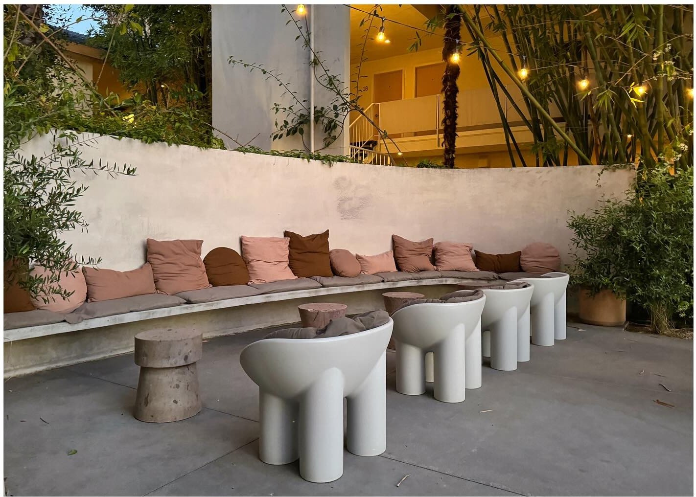 Courtyard banquette with pink cushions and cylindrical stone tables