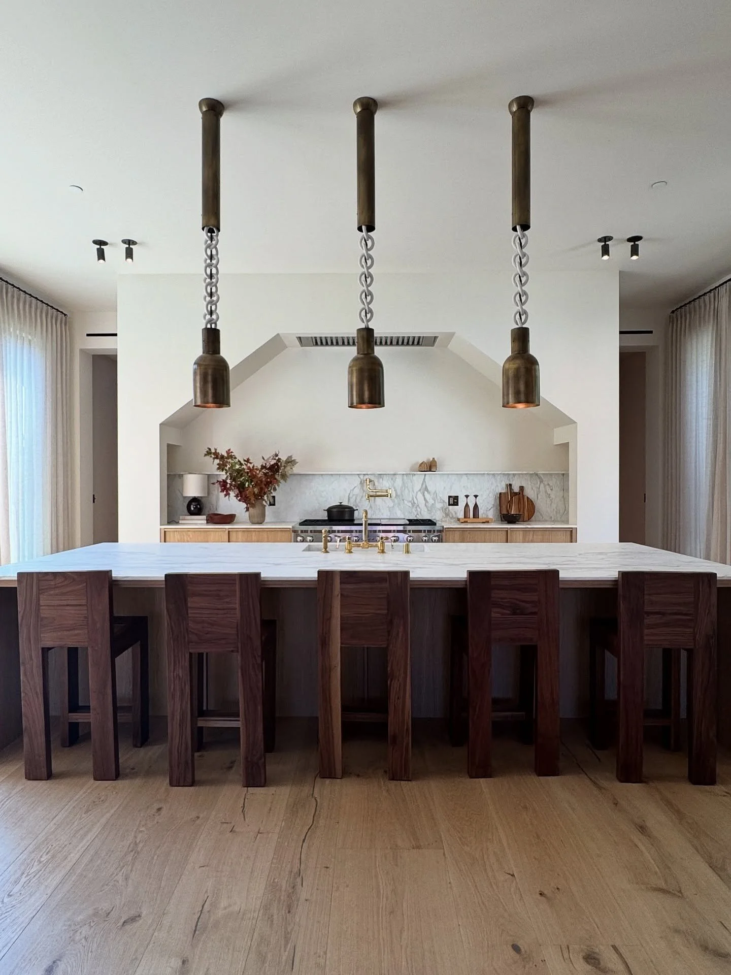 Kitchen island with dark red stools beneath suspended lights