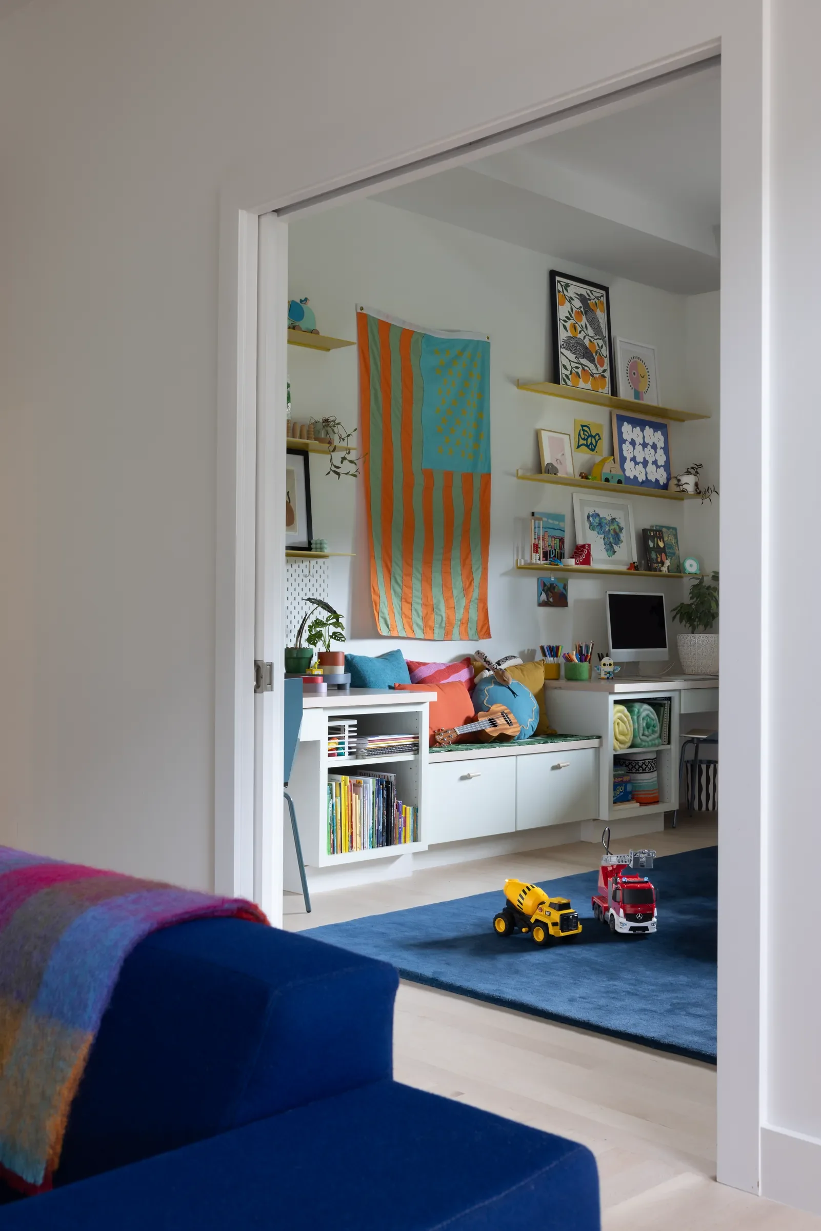 Colorful children’s playroom viewed through a doorway, with shelves, toys, and a blue rug.