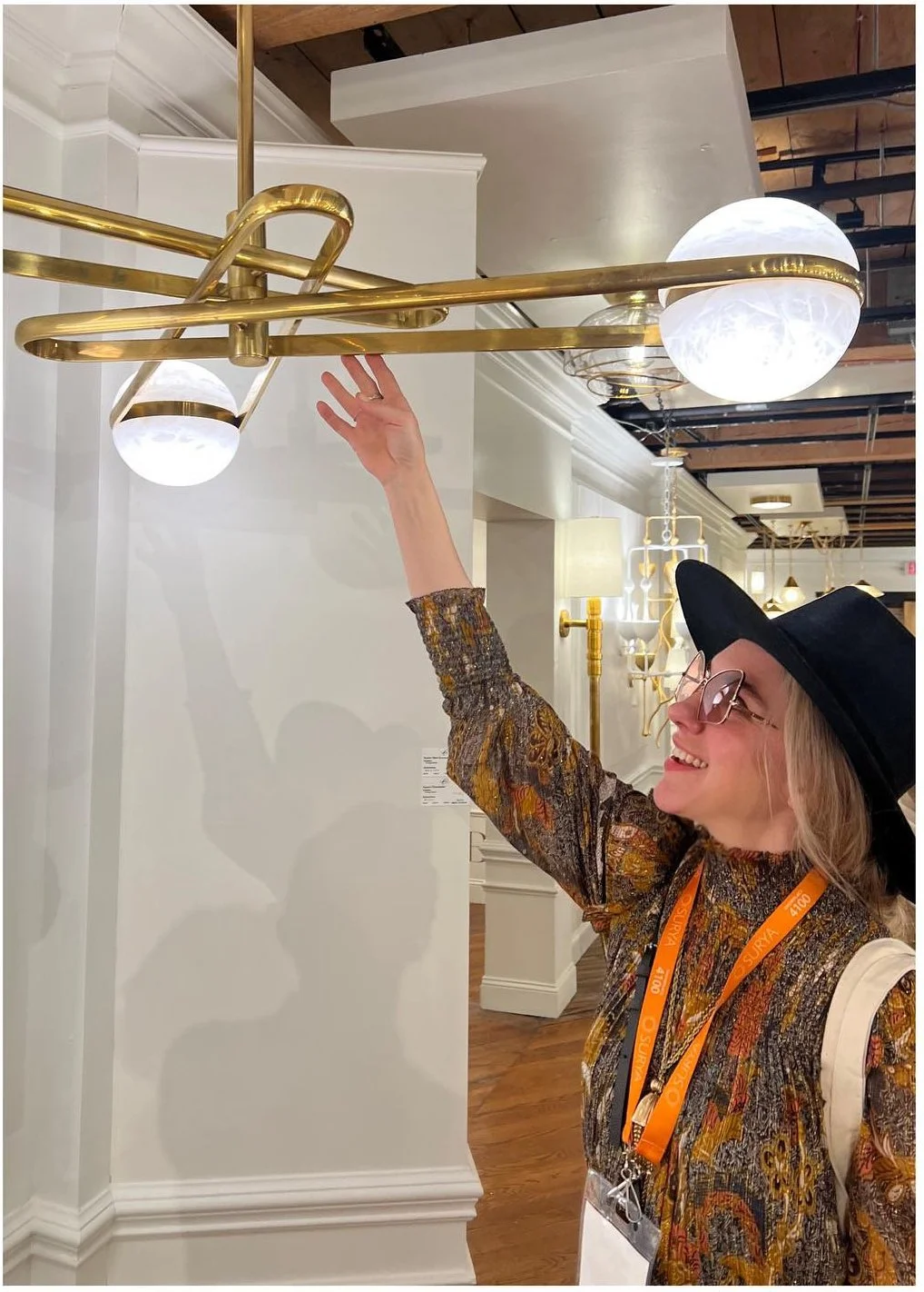 Designer inspecting a brass ceiling fixture with a white globe shade