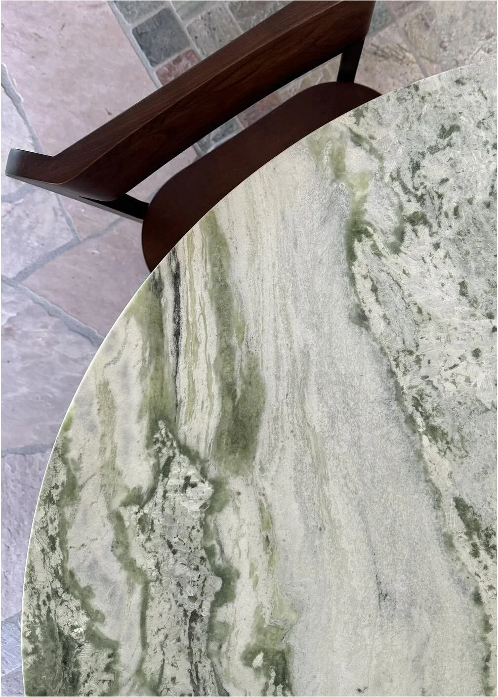 Close-up of a rounded green-veined stone table beside a wood chair