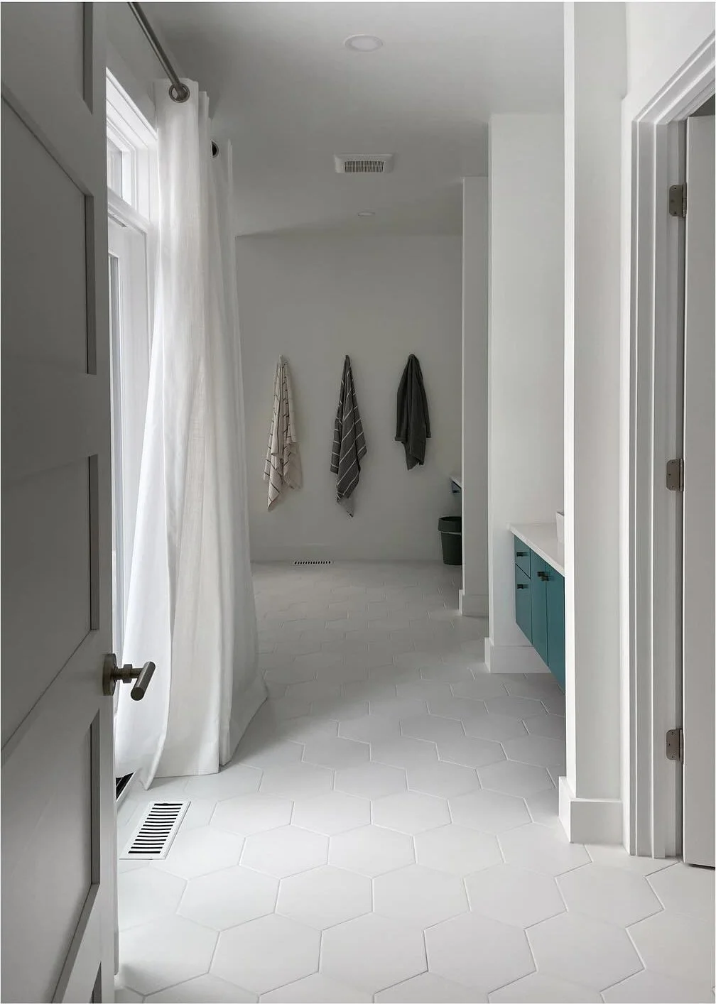 White bathroom corridor with a recessed bathtub and turquoise cabinetry