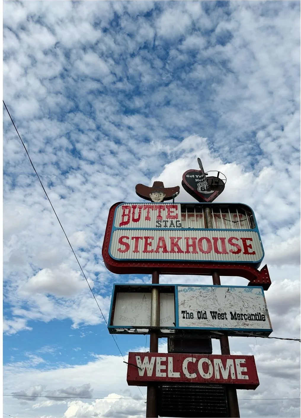Cowboy steakhouse sign with a hat-shaped topper beneath clouds