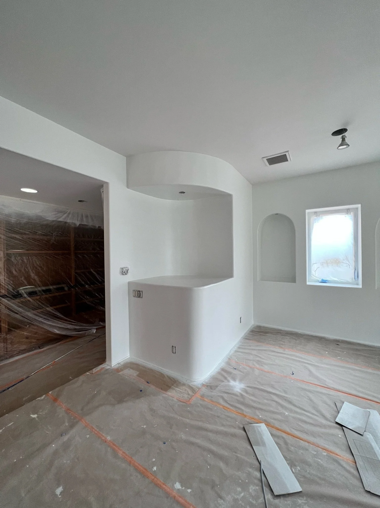 White room under renovation with curved wall details and protected floors.