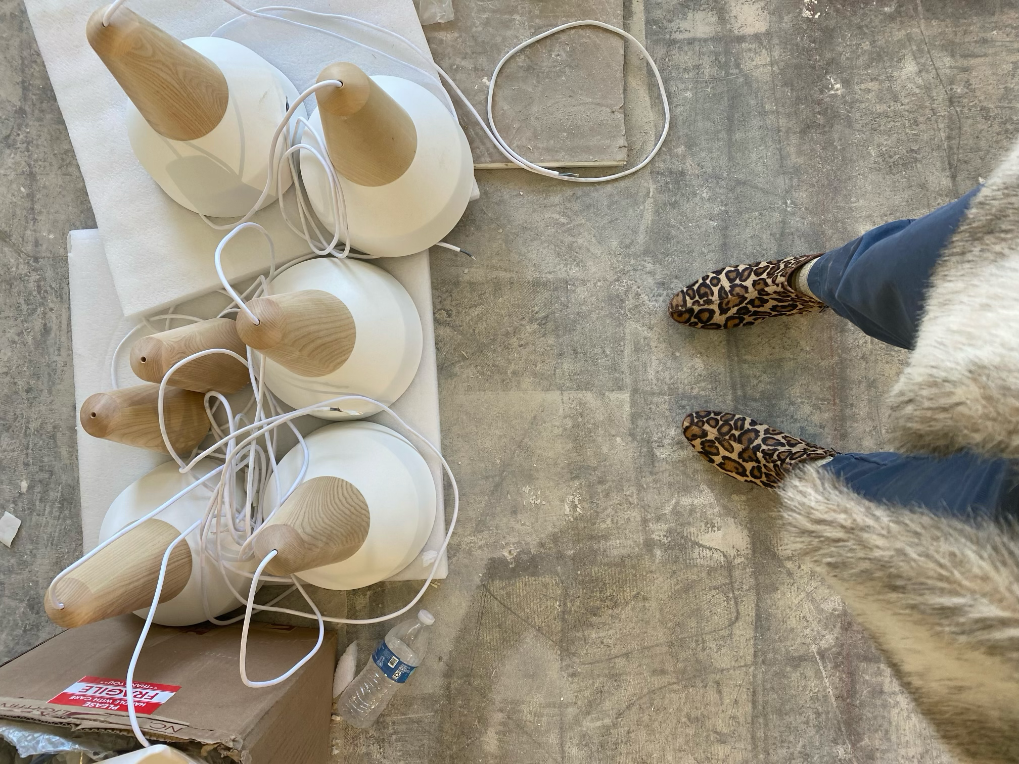 White and wood pendant lights on a concrete floor beside leopard-print shoes.