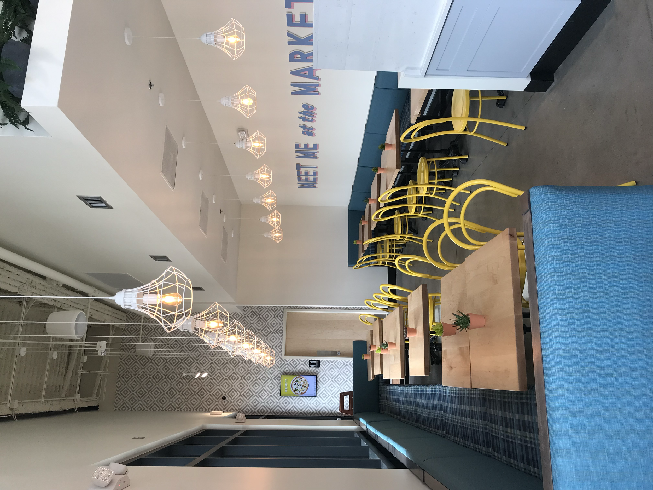 Restaurant dining area with yellow chairs, blue seating, wood tables, and pendant lights.