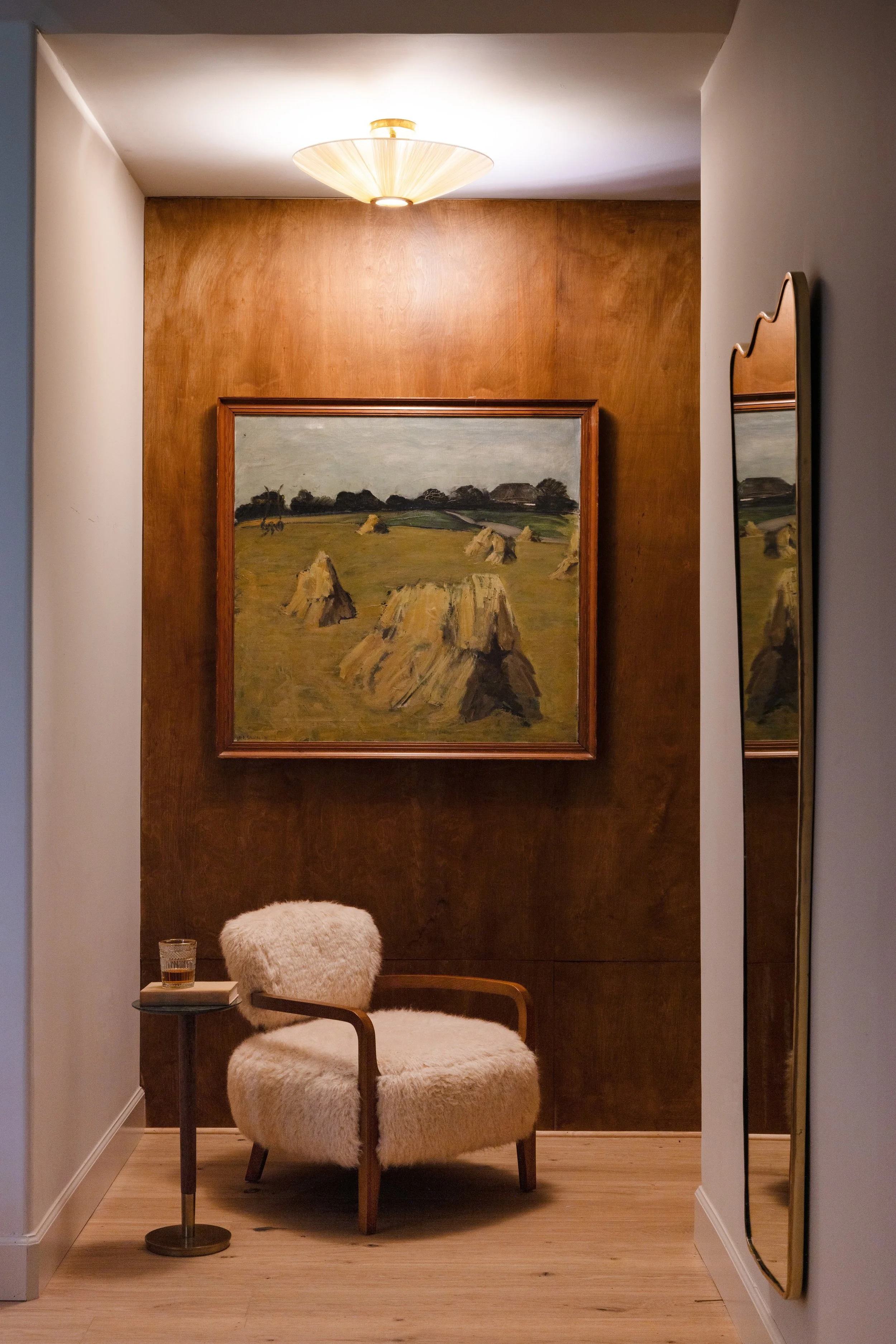 Wood-paneled alcove with a lounge chair and landscape painting.