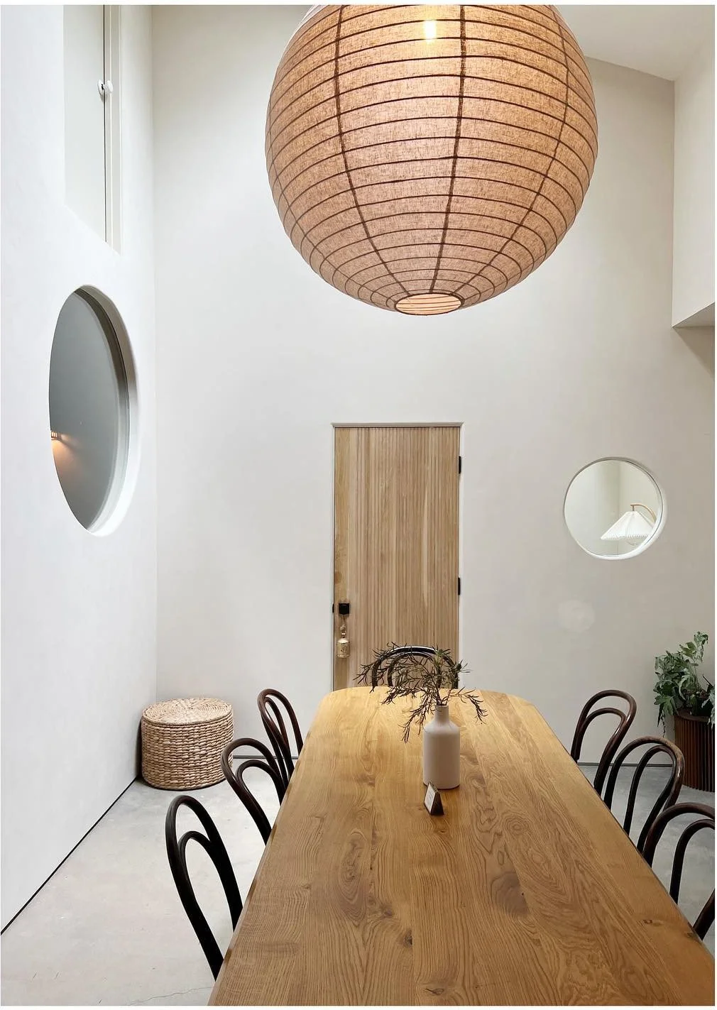 Long wood work table and black chairs beneath an oversized paper lantern