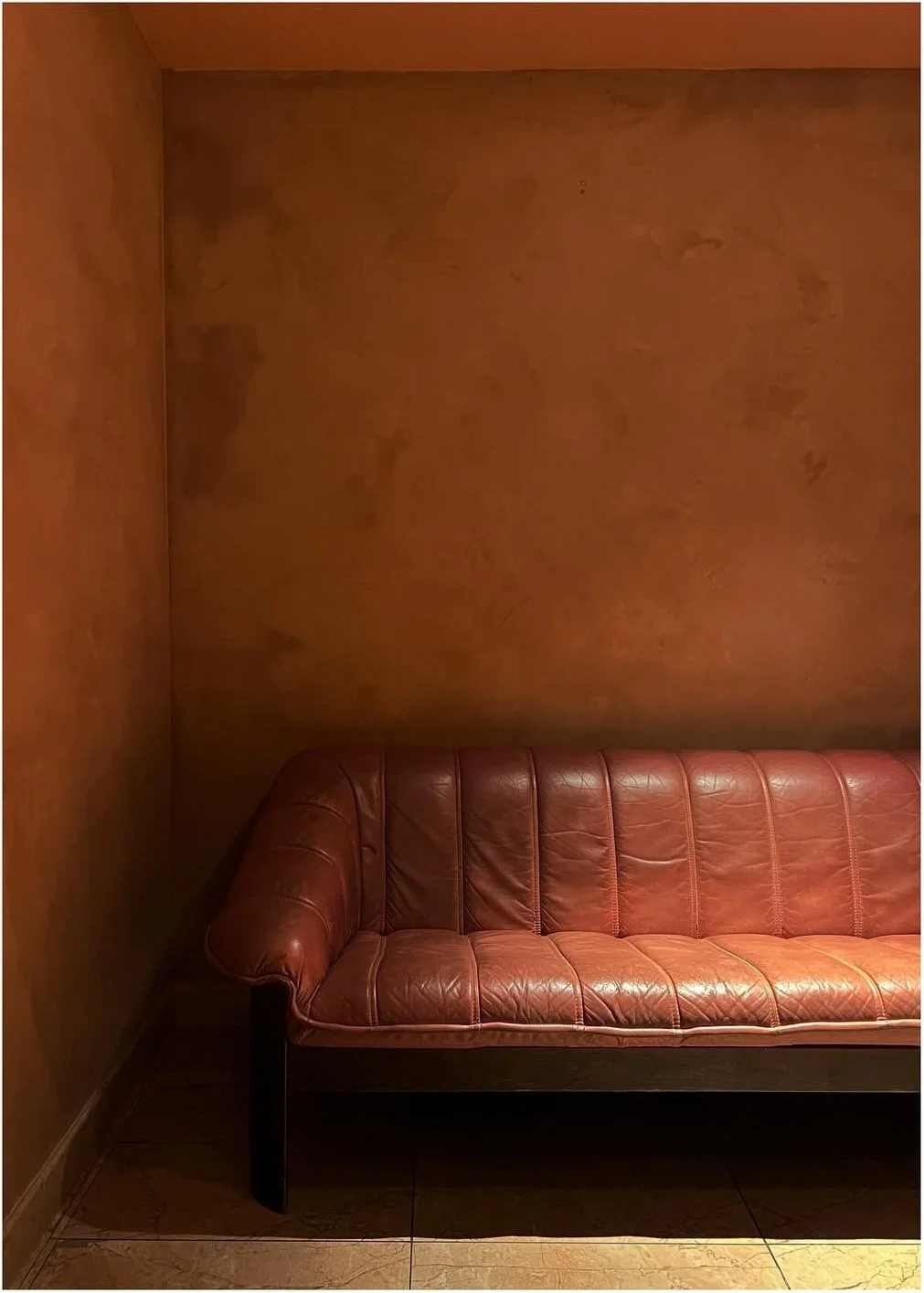 Red leather bench against a textured terracotta plaster wall