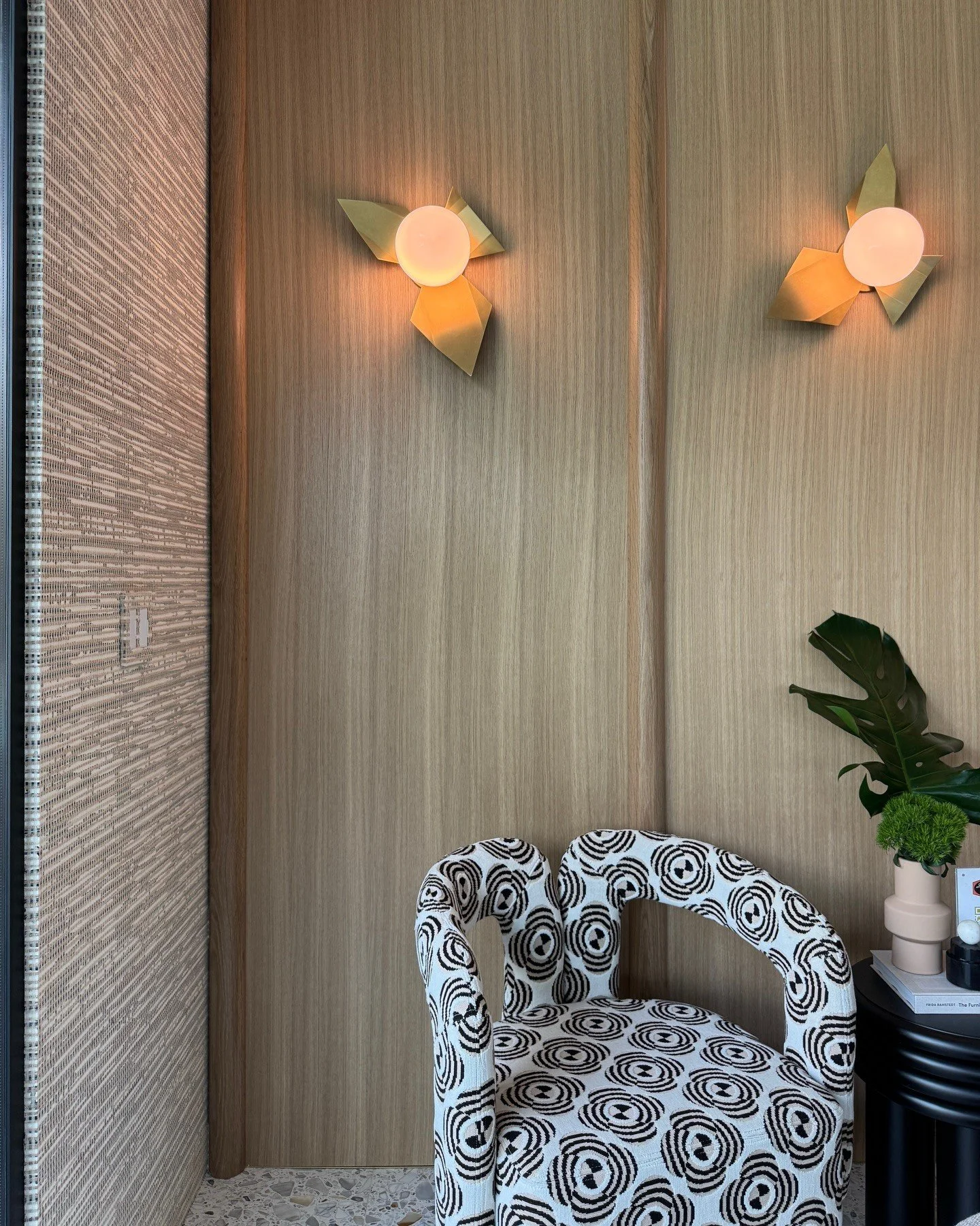 Patterned chair beneath floral wall sconces on wood paneling