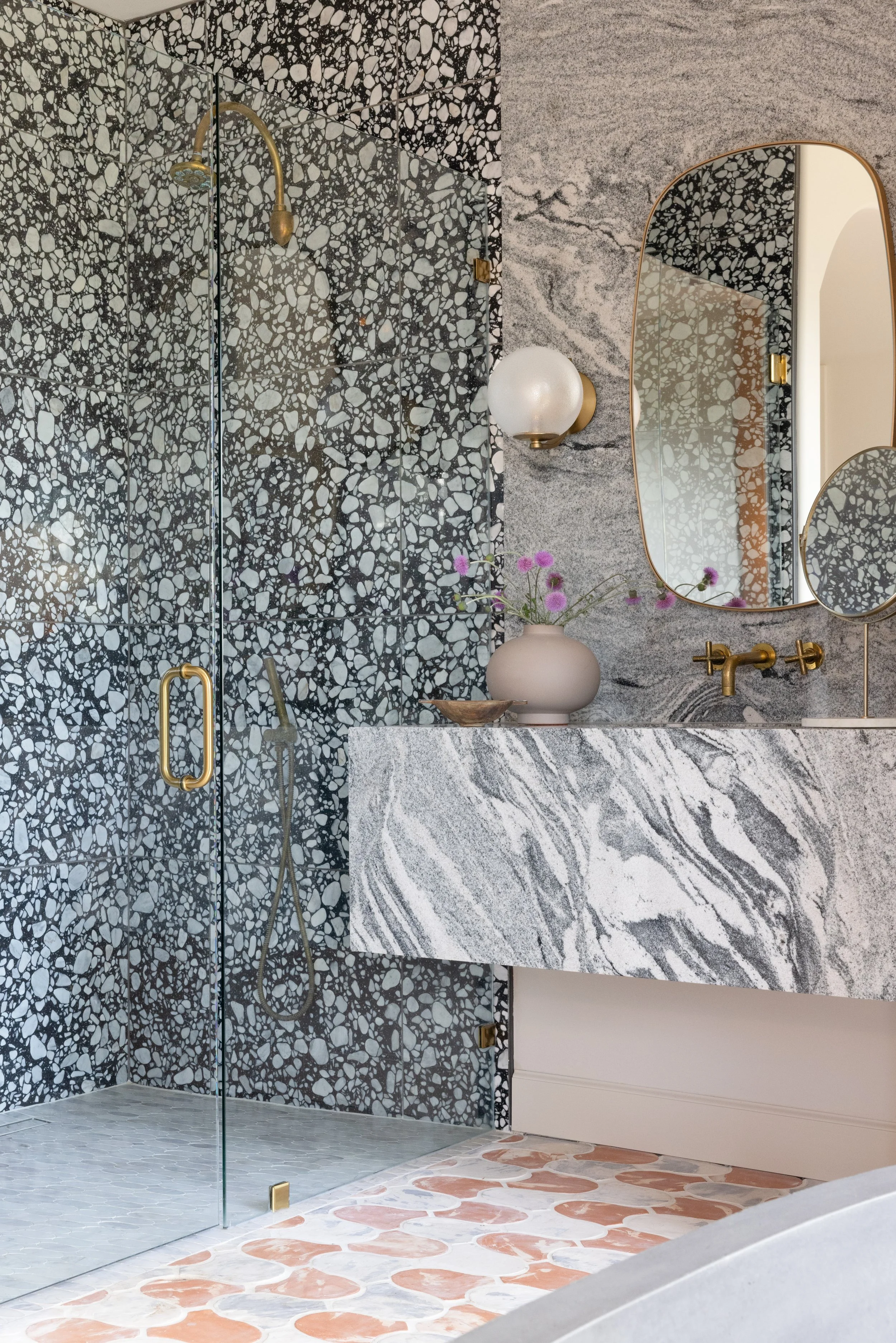 Bathroom with a veined stone vanity, arched mirror, and patterned shower tile.