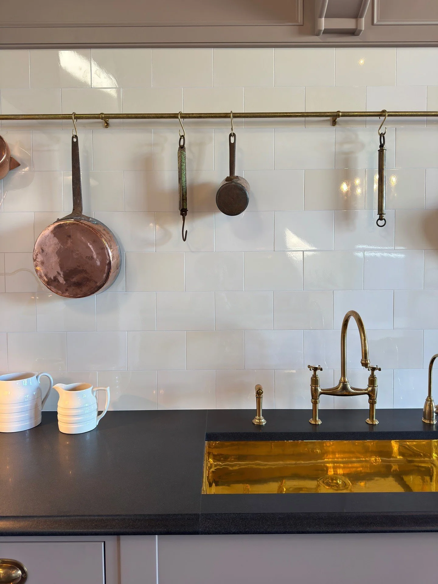 Brass sink and faucet beneath hanging copper pans