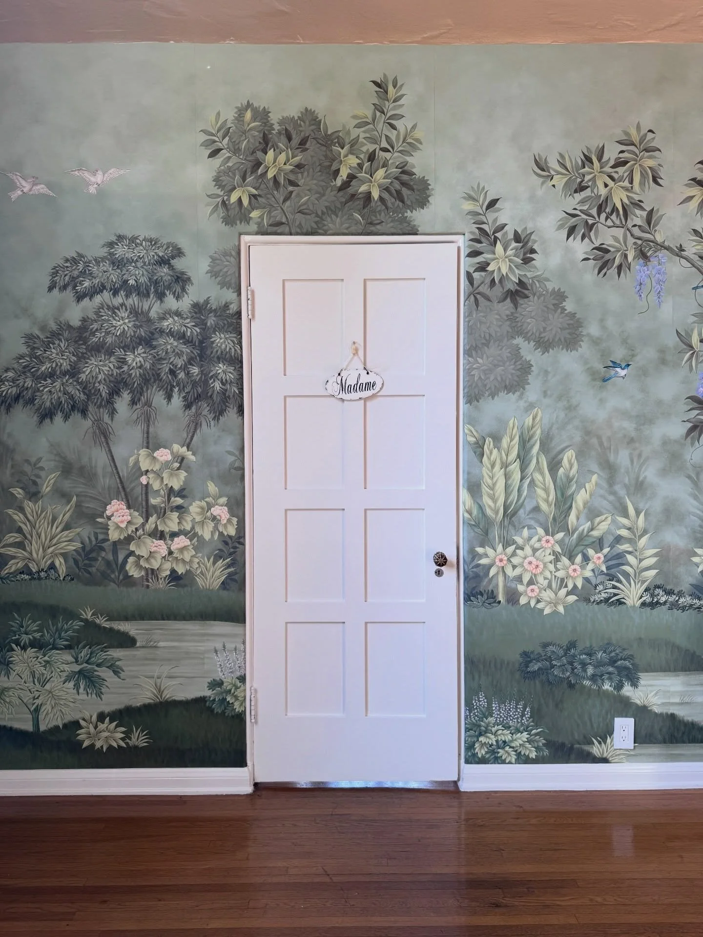 Pale door framed by a scenic botanical wall mural